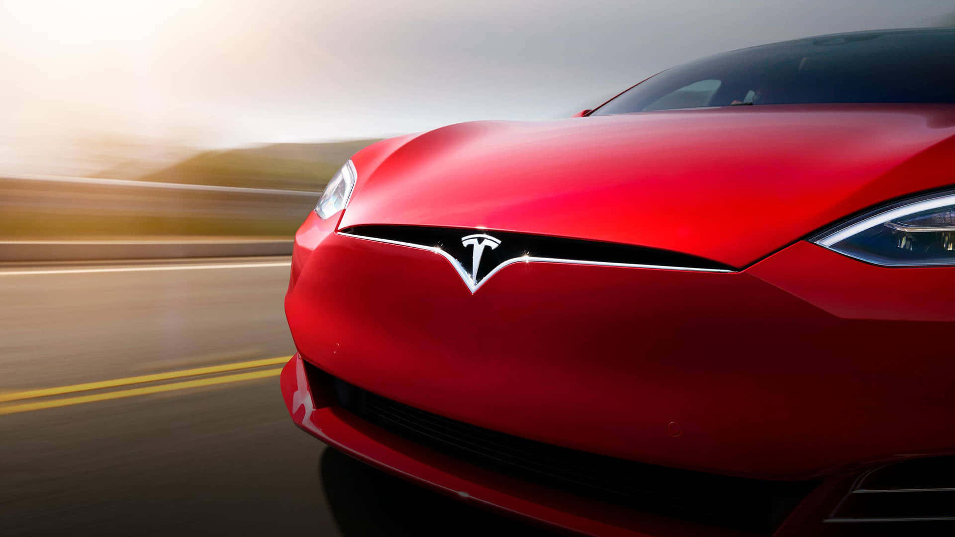 tesla 桌布 壁紙 — 一輛鮮紅色的Tesla在模糊的高速公路上奔馳，背景是朦朧的金色日出。