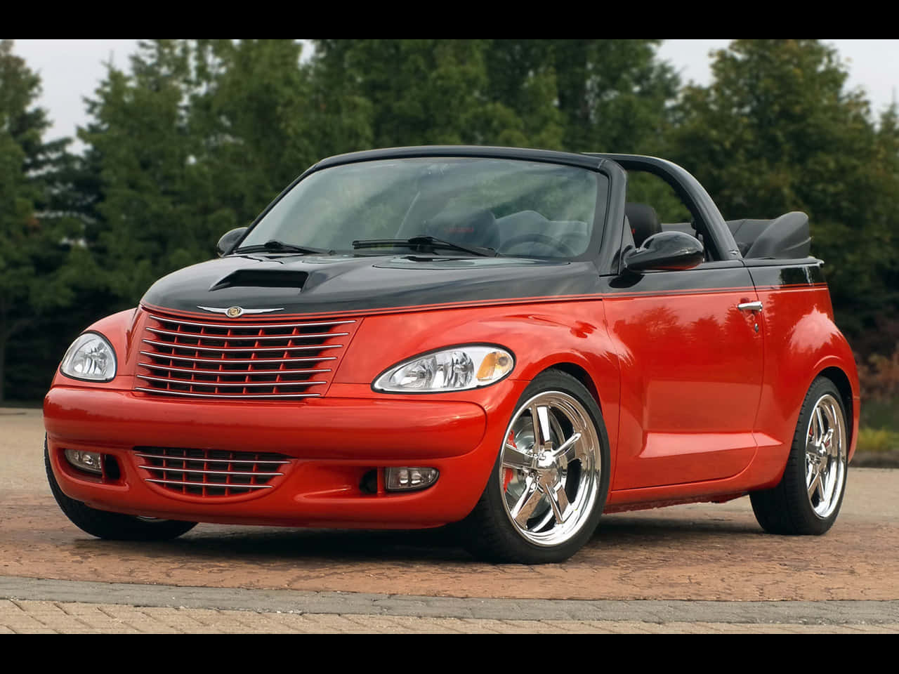 Chrysler Pt Cruiser 桌布 壁紙 — 一輛鮮紅色的克萊斯勒 PT Cruiser 敞篷車，黑色車頂，停泊在磚砌車道上，周圍綠樹成蔭。