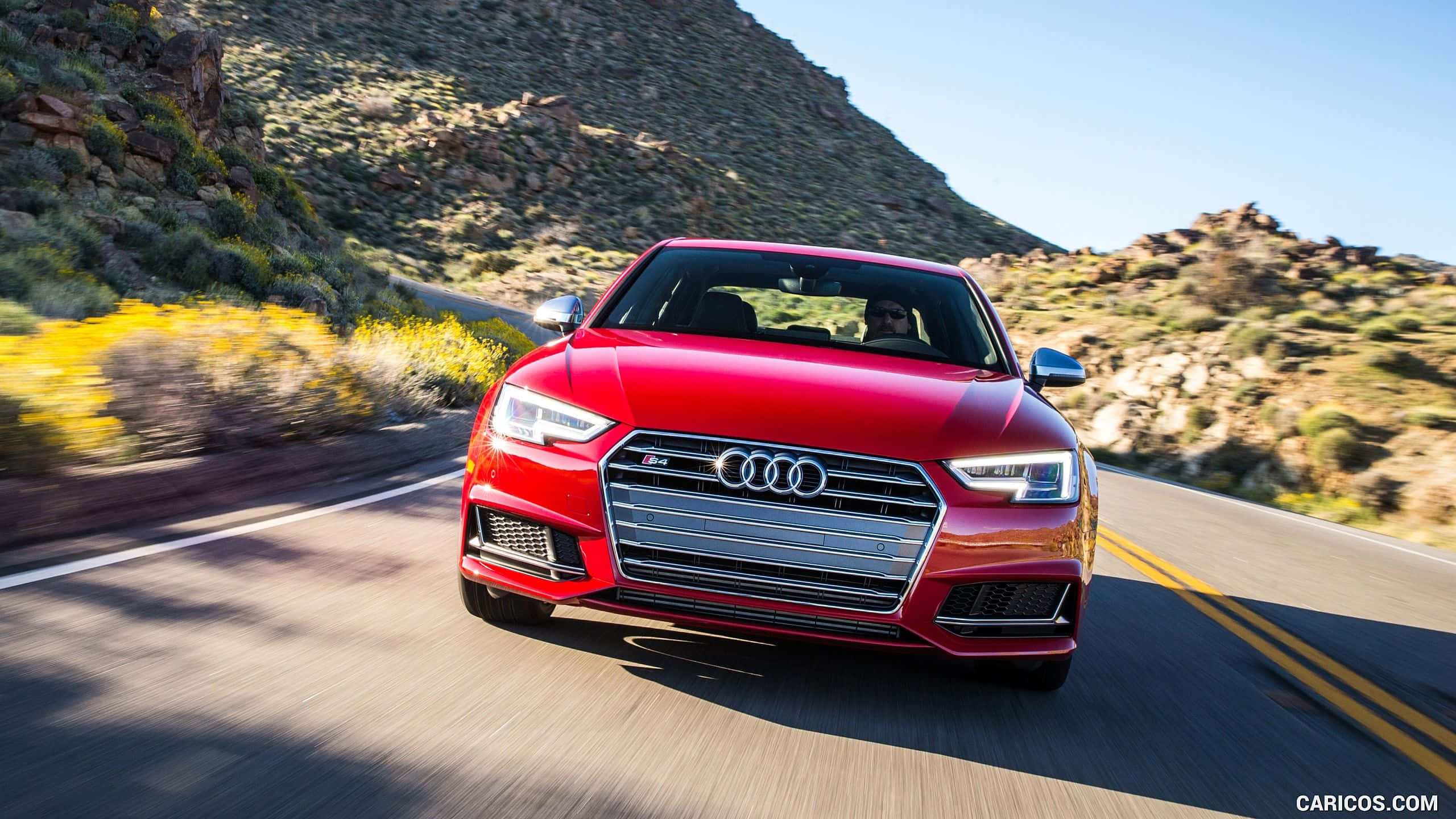 Audi S4 桌布 壁紙 — 一輛鮮紅色的奧迪S5在陽光明媚的沙漠公路上疾馳，帶有模糊的動態和岩石山坡。