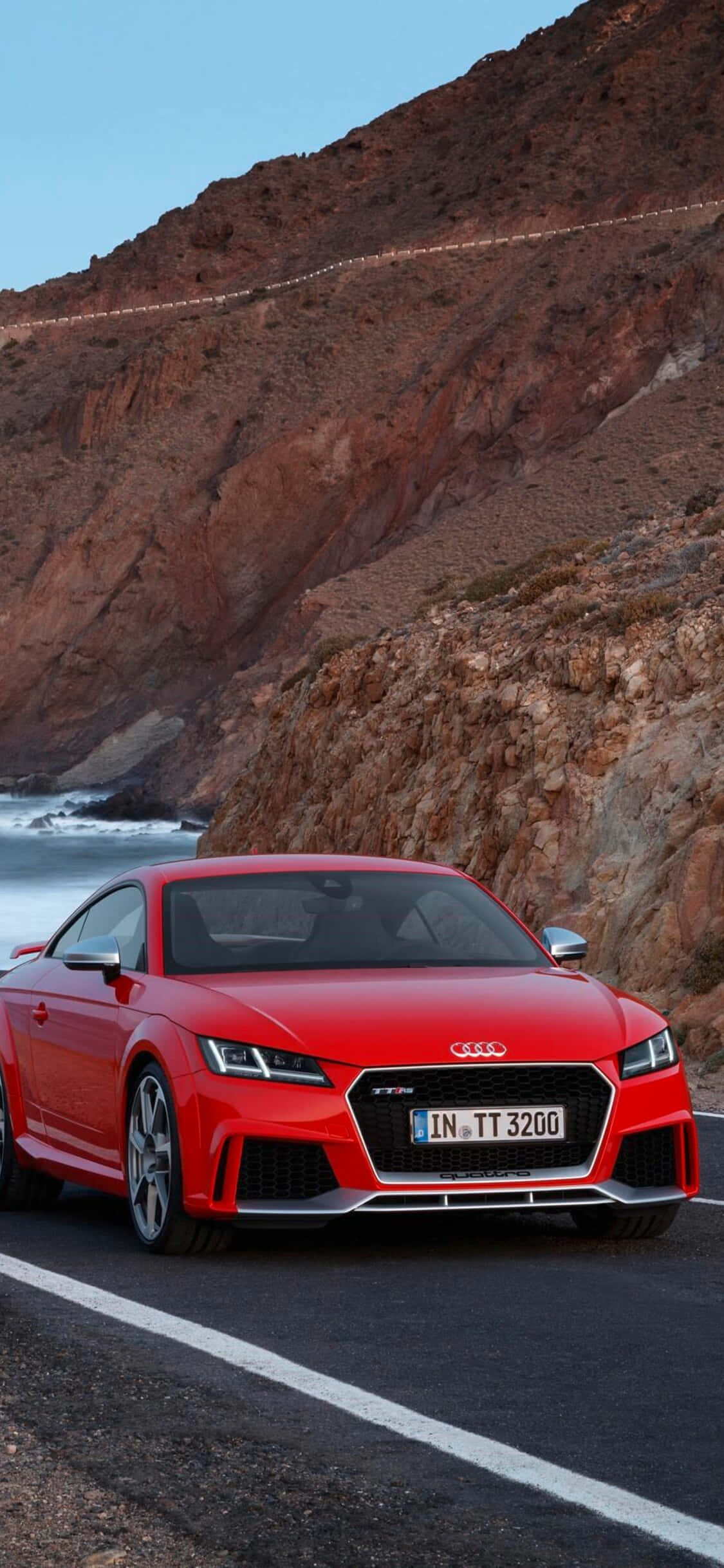 Audi Tt Rs 桌布 壁紙 — 一輛鮮紅色的奧迪TT RS跑車沿著海岸懸崖道路行駛，下方是崎嶇的懸崖和海洋波浪。
