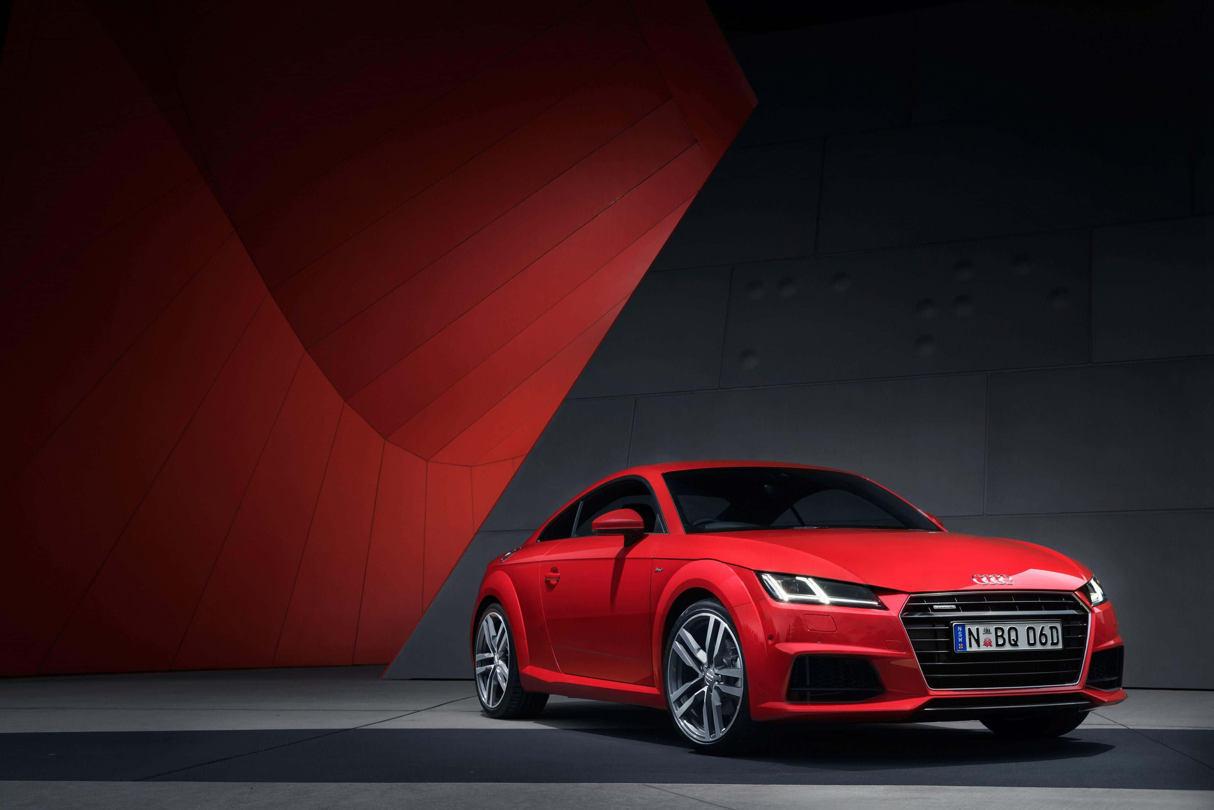 Audi Tt 桌布 壁紙 — 一輛鮮紅色的奧迪TT雙門跑車在攝影棚燈光下閃閃發光，背景是搶眼的紅色和深灰色幾何牆面。