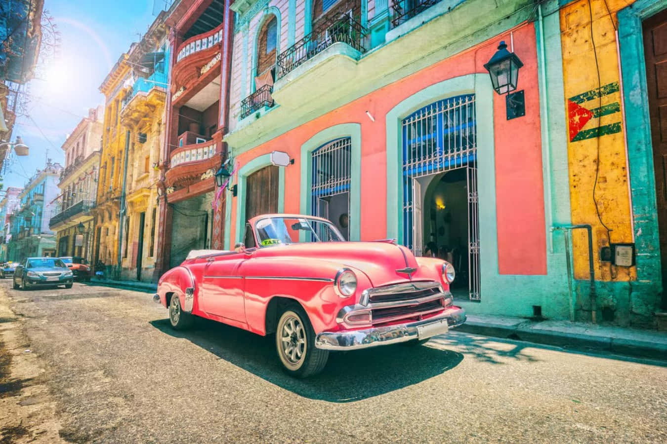 Cuba 桌布 壁紙 — 一輛鮮紅色的復古敞篷車停在古巴一條陽光普照、兩旁色彩繽紛的殖民建築的街道上。