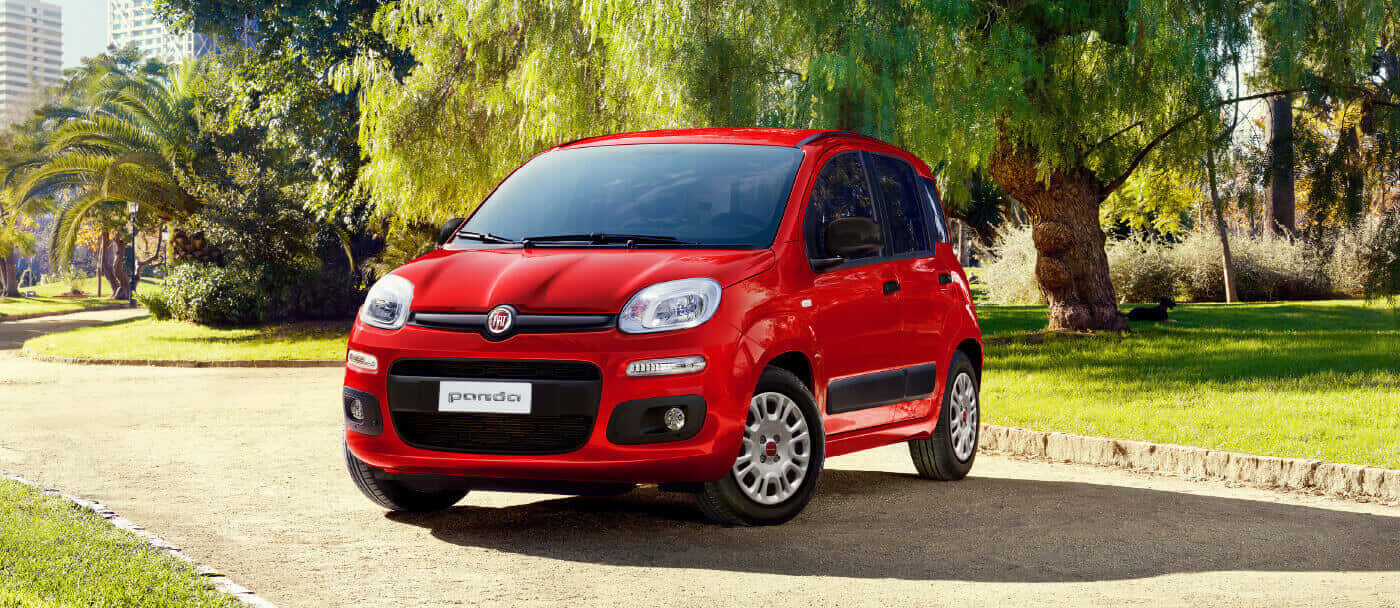 Fiat Panda 桌布 壁紙 — 一輛鮮紅色的快意 Panda 停泊在陽光普照的鋪砌小徑上，旁邊是茂密的綠草和枝葉繁茂的樹木。