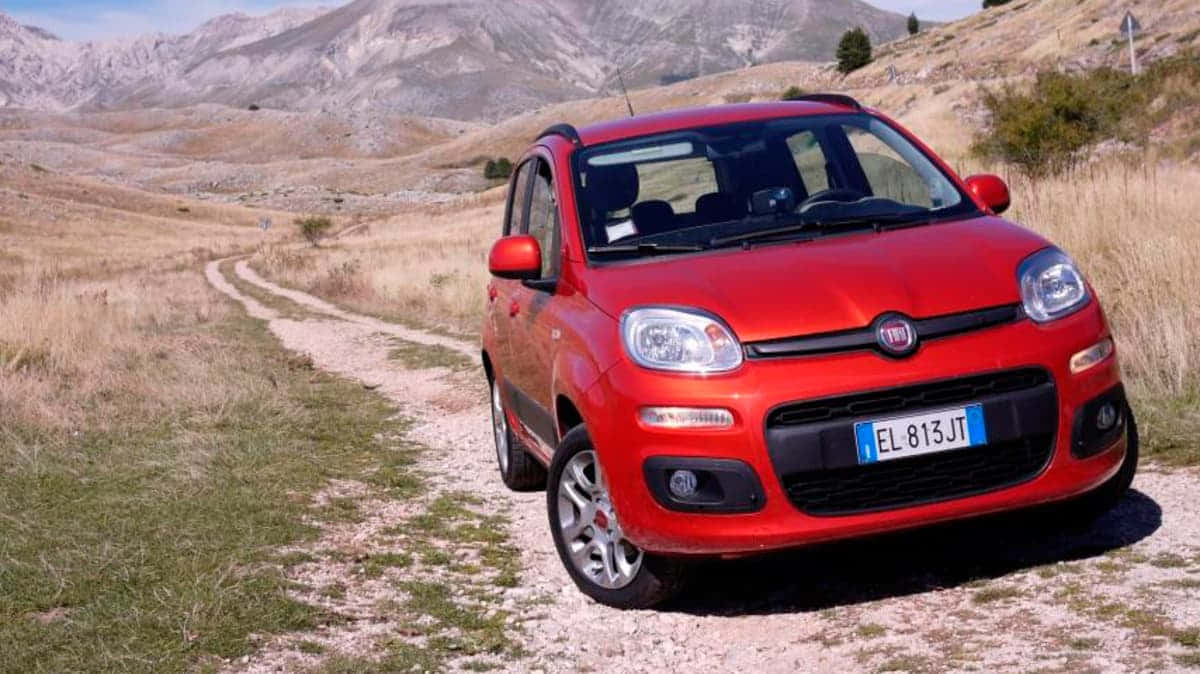 Fiat Panda 桌布 壁紙 — 一輛鮮紅色的快意 Panda 停泊在蜿蜒的泥路上，穿越乾燥的草原，背景是崎嶇的山脈。