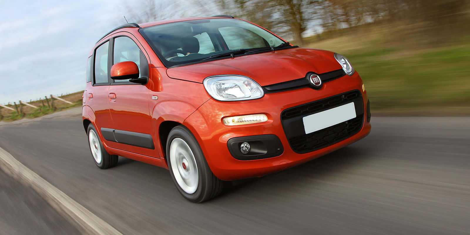 Fiat Panda 桌布 壁紙 — 一輛鮮紅色的快意 Panda 在鄉村道路上快速行駛，背景是模糊的綠化和多雲的天空。