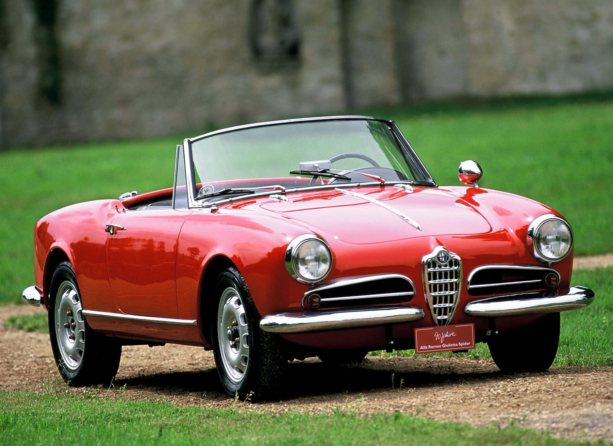 Alfa Romeo Spider 桌布 壁紙 — 一輛鮮紅色的愛快羅密歐Giulietta Spider開篷車停在草地上，背景是石牆。