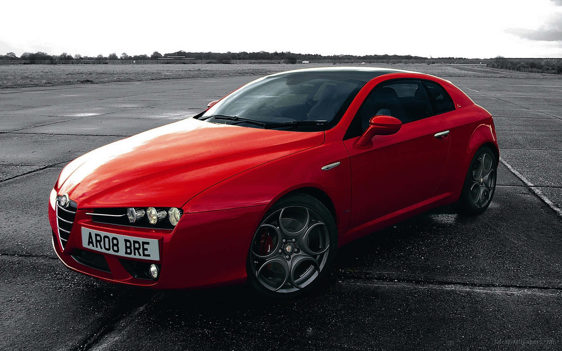 Alfa Romeo Brera 桌布 壁紙 — 一輛鮮紅色的愛快羅密歐跑車在潮濕的瀝青跑道上，於多雲的天空下閃閃發光。