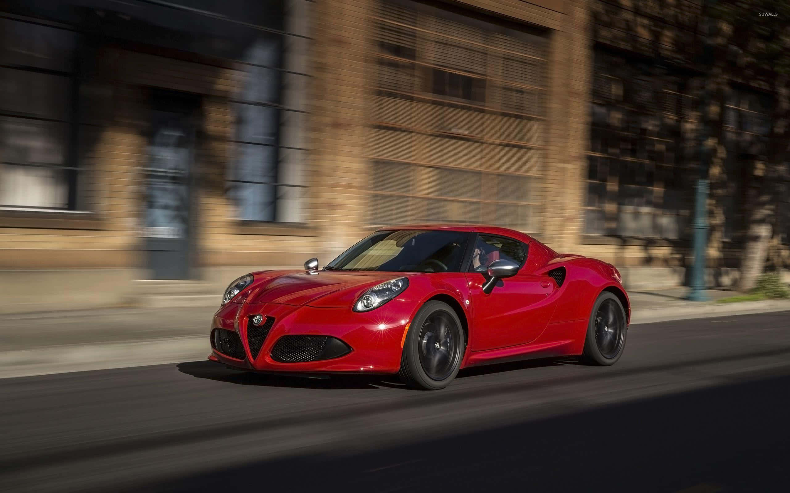 Alfa Romeo 4c 桌布 壁紙 — 一輛鮮紅色的愛快羅密歐跑車在陽光明媚的城市街道上疾馳，背景建築物呈現動態模糊效果。