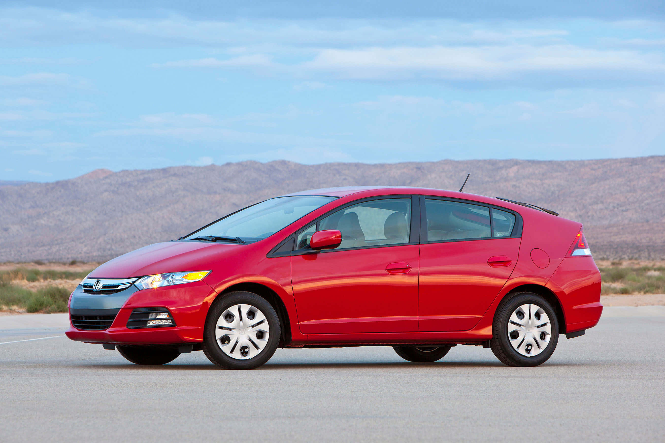 Honda Insight 桌布 壁紙 — 一輛鮮紅色的本田Insight混合動力車停在瀝青路上，背景是乾燥的山脈和淡藍色的天空。