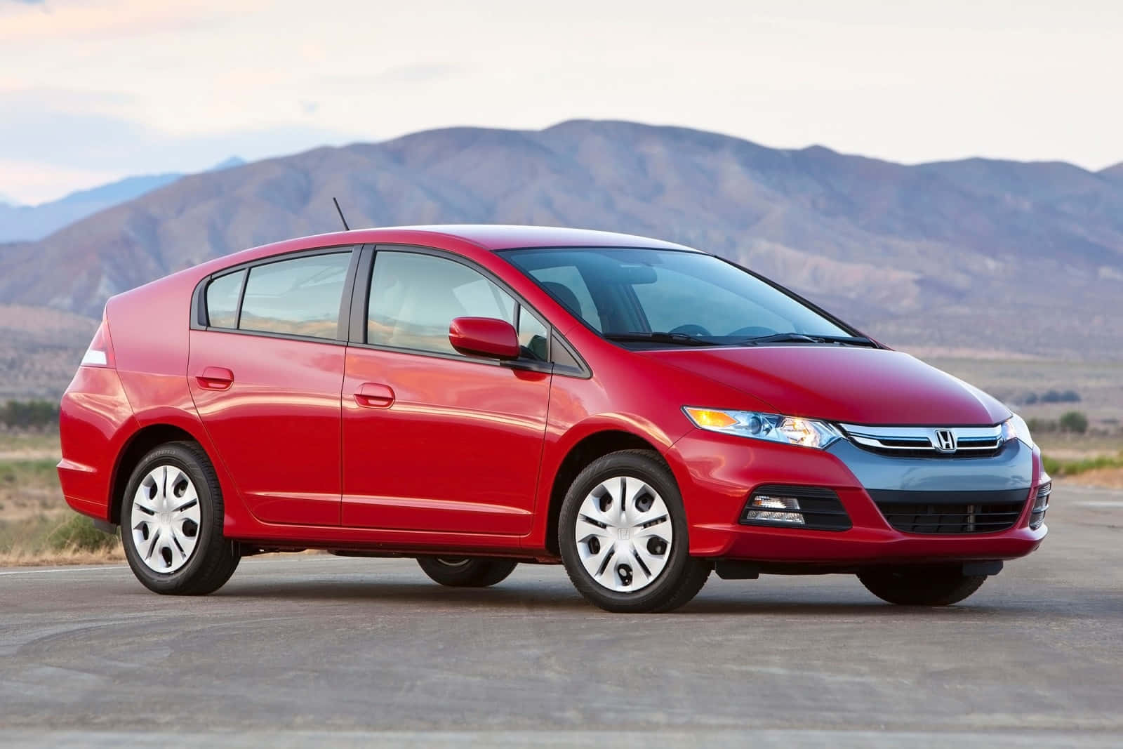 Honda Insight 桌布 壁紙 — 一輛鮮紅色的本田Insight混合動力車停在鋪砌的道路上，遠處有山巒，天空柔和。