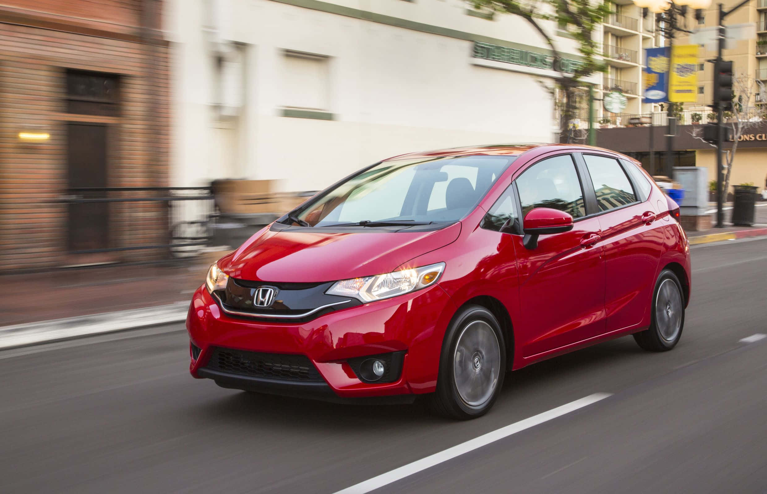 Honda Fit 桌布 壁紙 — 一輛鮮紅色的本田飛度在城市街道上行駛，建築物和路面呈現動態模糊效果。