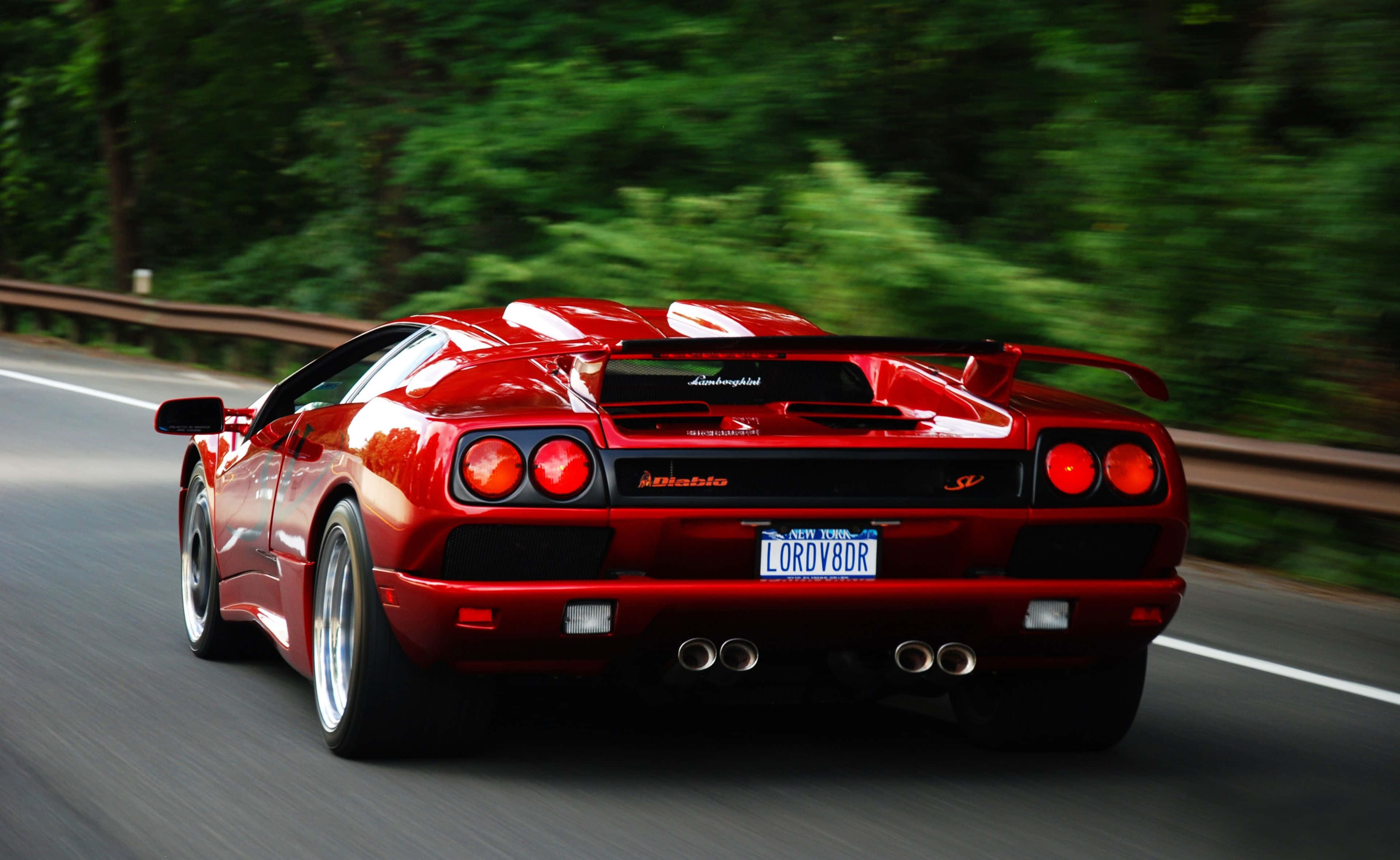 Lamborghini Diablo 桌布 壁紙 — 一輛鮮紅色的林寶堅尼 Diablo 在森林大道上疾馳，動態模糊效果突顯其力量與流線型設計。