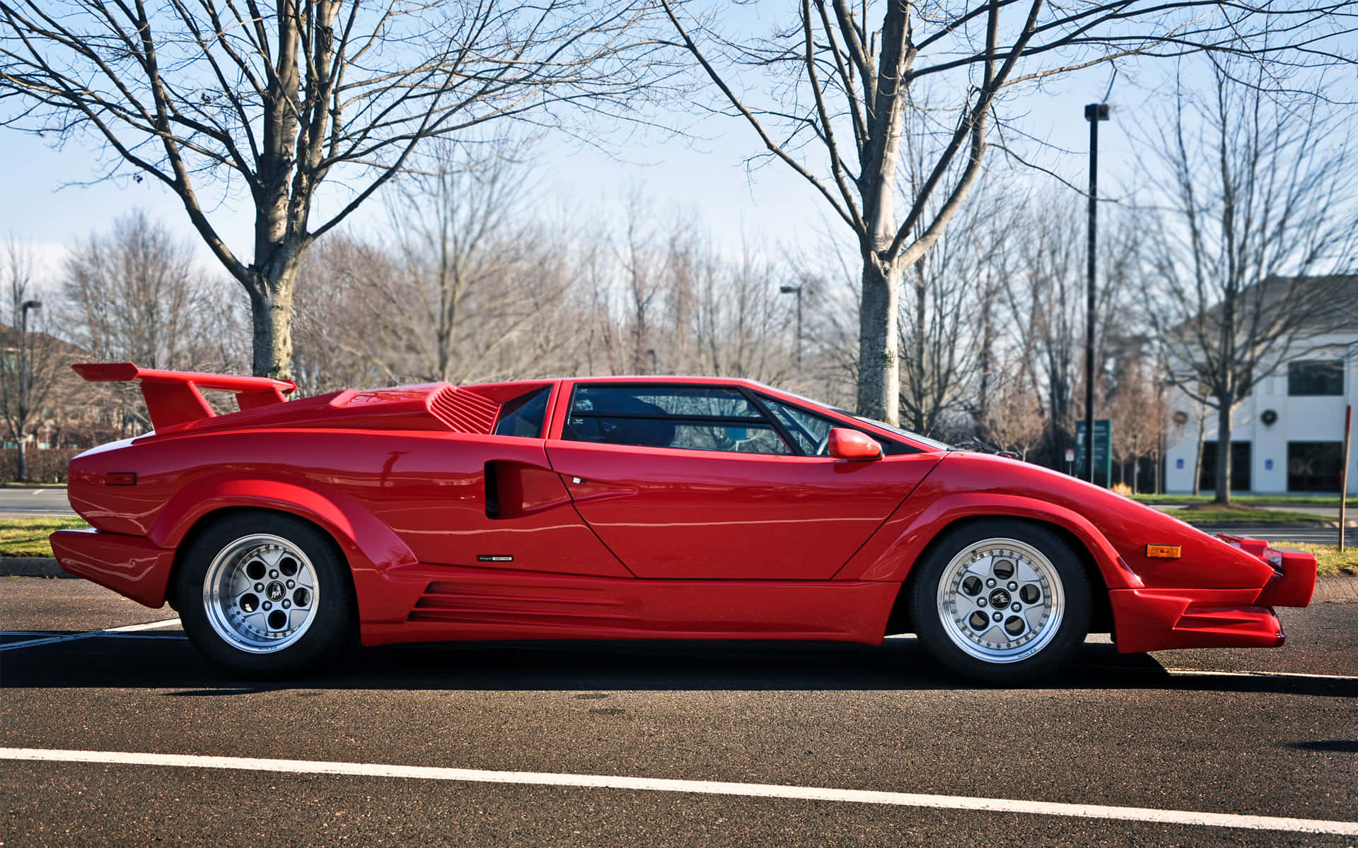 Lamborghini Countach 桌布 壁紙 — 一輛鮮紅色的林寶堅尼Countach停泊在瀝青路上，周圍是光禿禿的樹木，天空清澈湛藍。