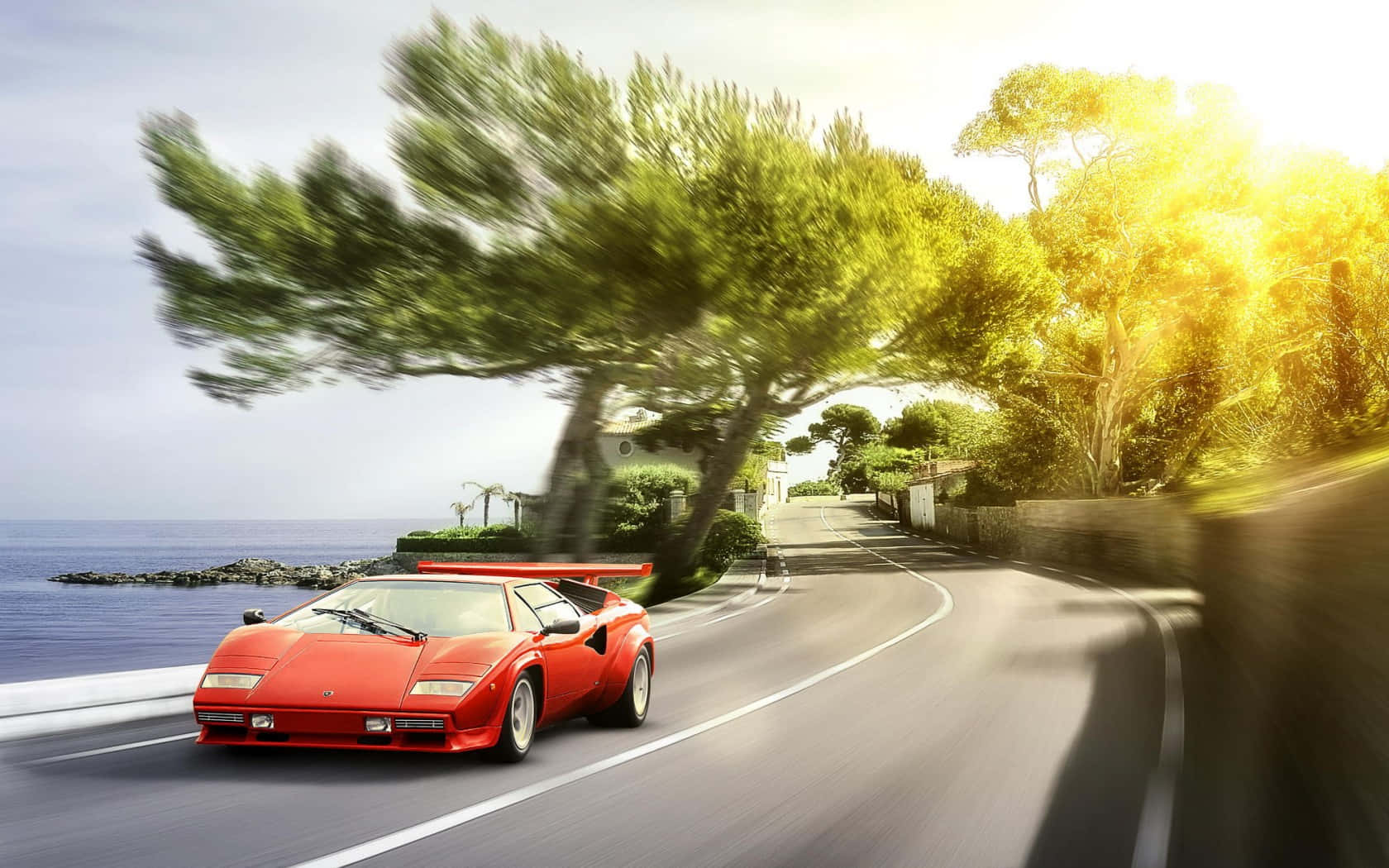 Lamborghini Countach 桌布 壁紙 — 一輛鮮紅色的林寶堅尼Countach沿著海岸公路飛馳，背景是模糊的樹木和動態的海洋。