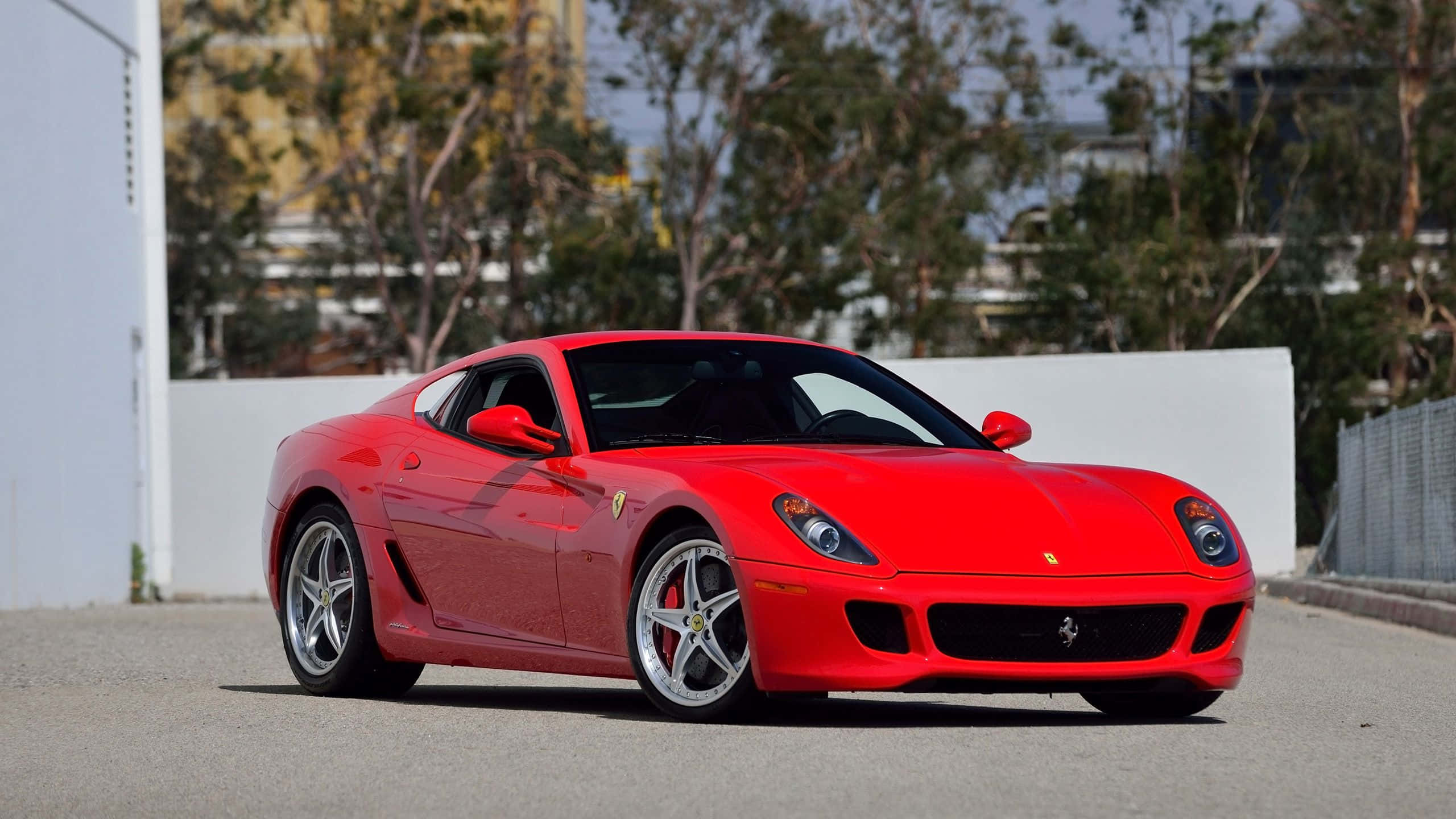 Ferrari 599 Gtb Fiorano 桌布 壁紙 — 一輛鮮紅色的法拉利 599 GTB Fiorano 停泊在鋪砌路面上，背景有樹木和白色牆壁。