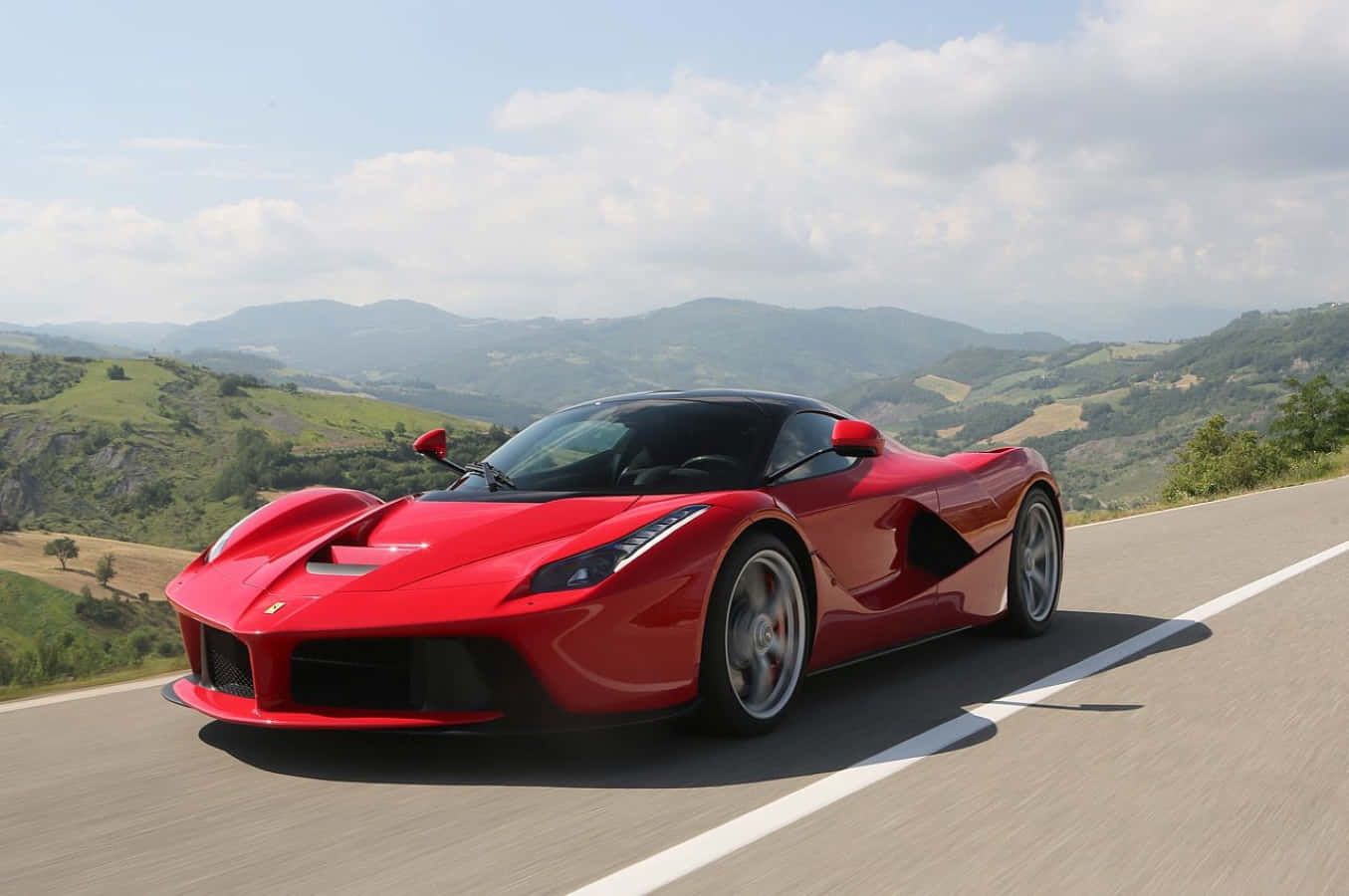 Ferrari Laferrari 桌布 壁紙 — 一輛鮮紅色的法拉利 LaFerrari 在部分多雲的天空下，沿著蜿蜒的山路飛馳。