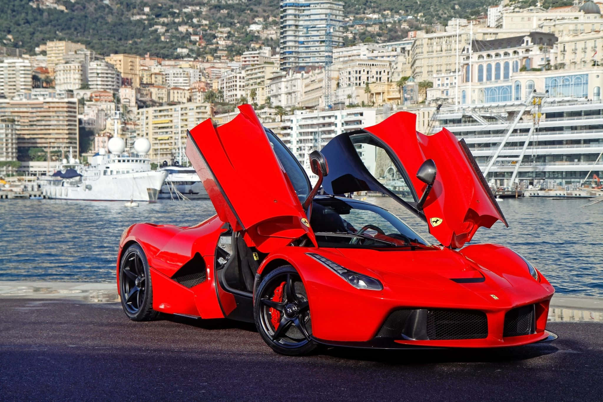 Ferrari Laferrari 桌布 壁紙 — 一輛鮮紅色的法拉利 LaFerrari 打開鷗翼車門，停泊在海濱長廊上，俯瞰著停滿豪華遊艇的港口和密集的沿海城市景觀。