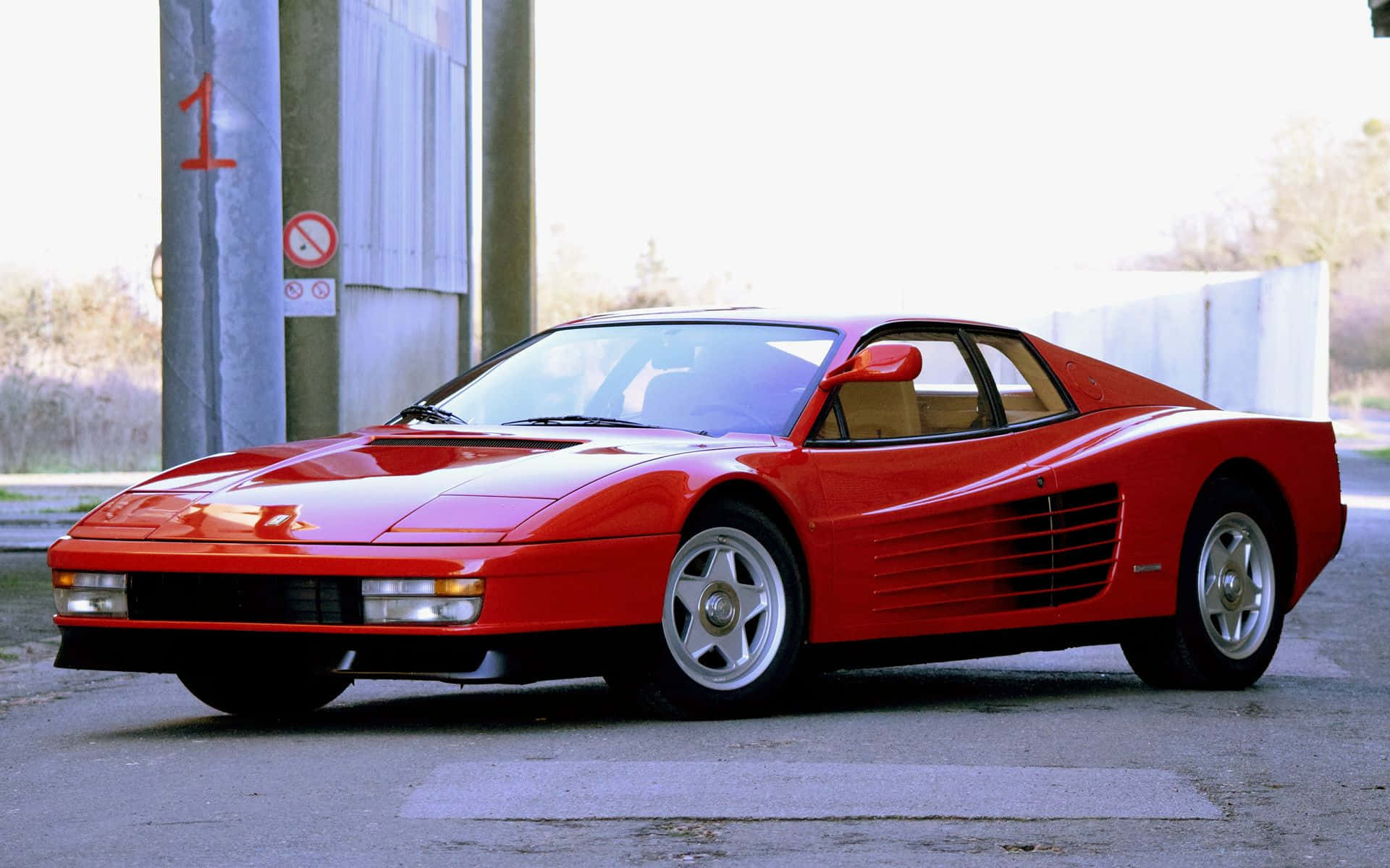 Ferrari Testarossa 桌布 壁紙 — 一輛鮮紅色的法拉利 Testarossa 停在加油站，背景是明亮的天空和工業環境。
