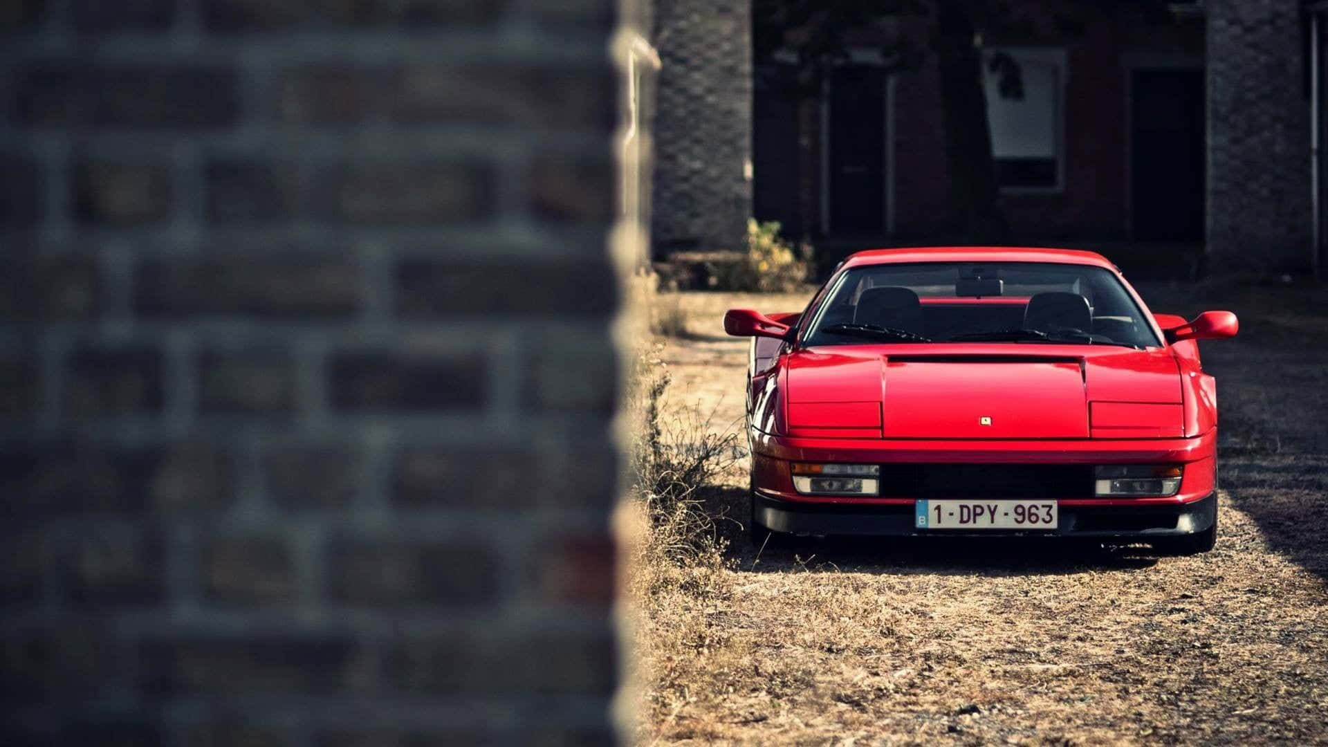 Ferrari Testarossa 桌布 壁紙 — 一輛鮮紅色的法拉利288 GTO在明亮的日光下停泊在磚牆之間的乾草地上。