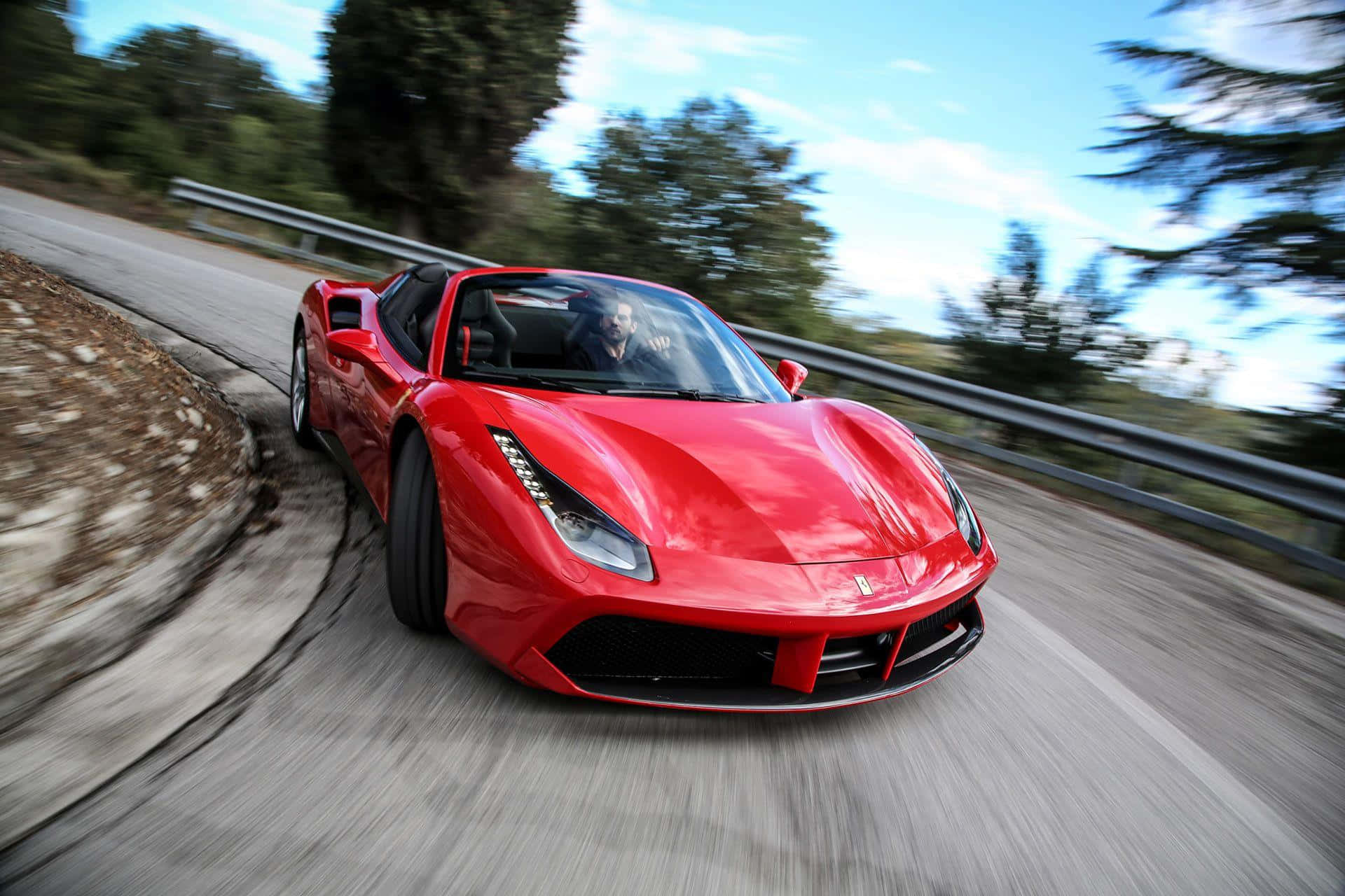 Ferrari 488 Spider 桌布 壁紙 — 一輛鮮紅色的法拉利488 Spider在蜿蜒的山路上飛馳，背景是模糊的綠樹和藍天。