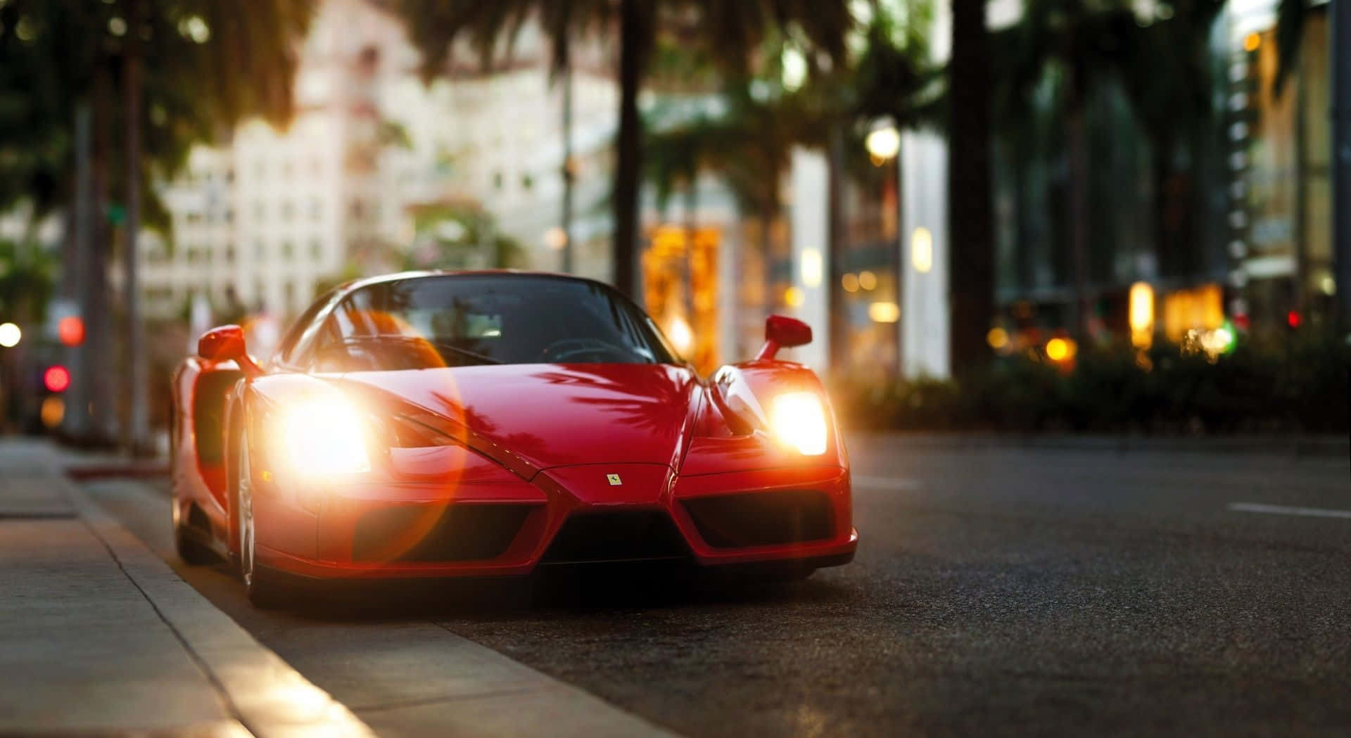 Ferrari Enzo 桌布 壁紙 — 一輛鮮紅色的法拉利Enzo亮著車頭燈閃閃發光，停泊在黃金時段棕櫚樹成蔭的城市街道上。
