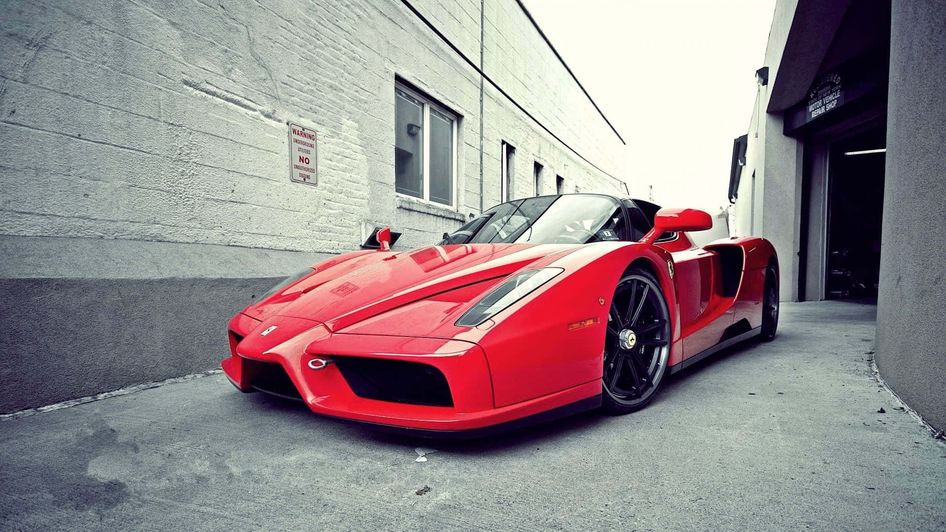 Ferrari Enzo 桌布 壁紙 — 一輛鮮紅色的法拉利Enzo停泊在灰色混凝土建築之間的狹窄小巷中，天空多雲。