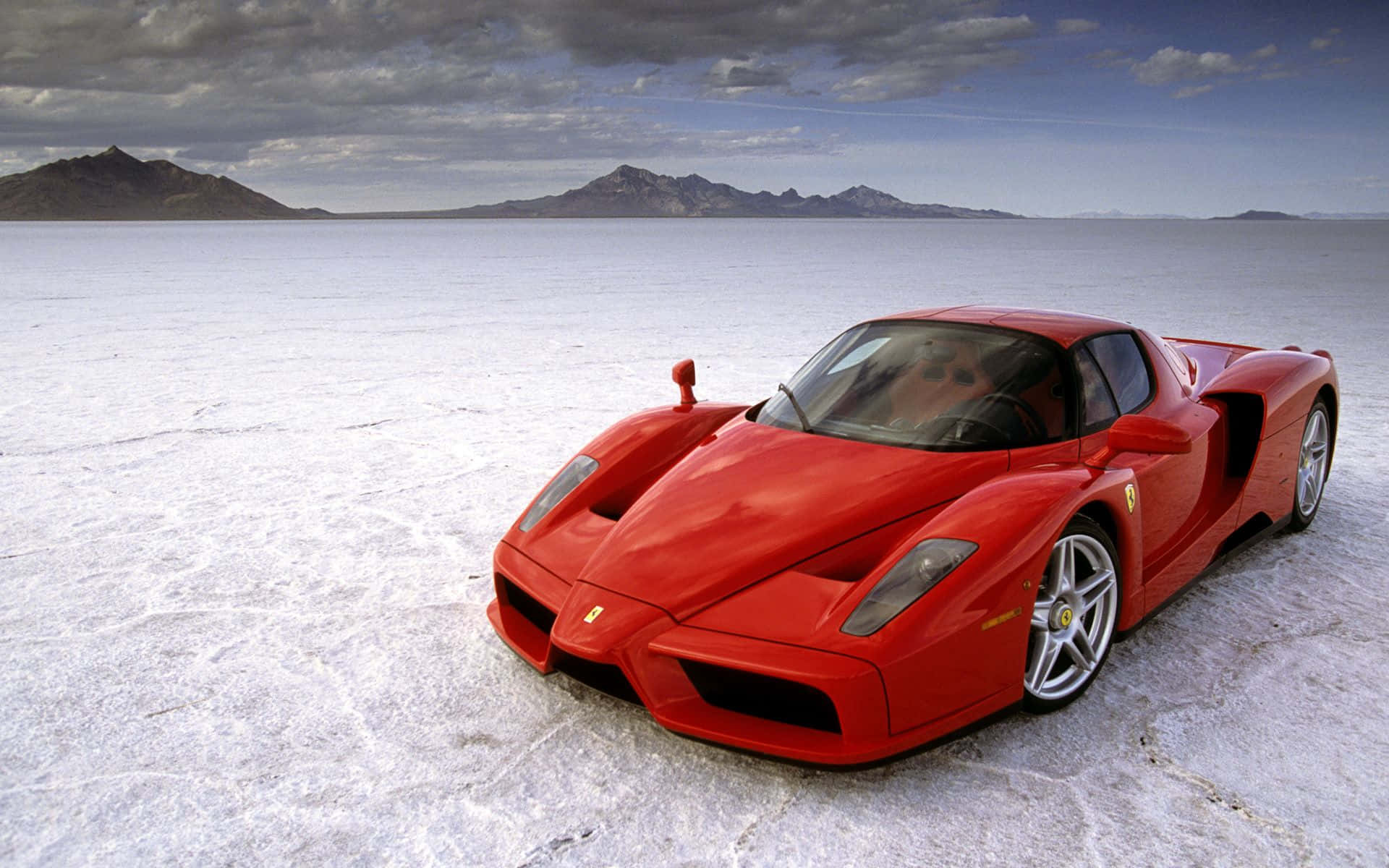 Ferrari Enzo 桌布 壁紙 — 一輛鮮紅色的法拉利Enzo獨自停在一片廣闊的白色鹽灘上，遠處有山脈，天空多雲。