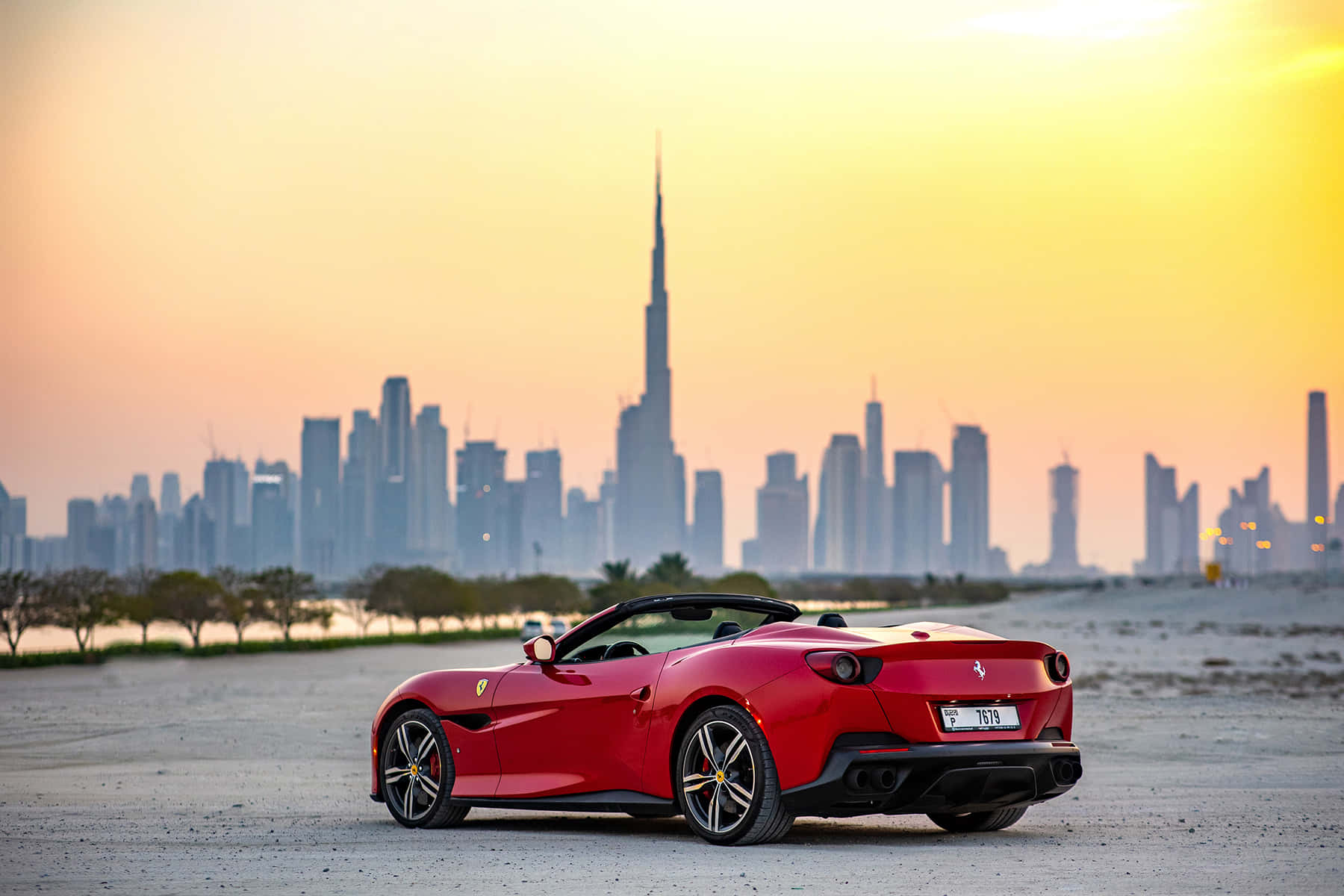 Ferrari Portofino 桌布 壁紙 — 一輛鮮紅色的法拉利Portofino停在沙漠平原上，杜拜的天際線和哈里發塔在金色夕陽中閃耀。