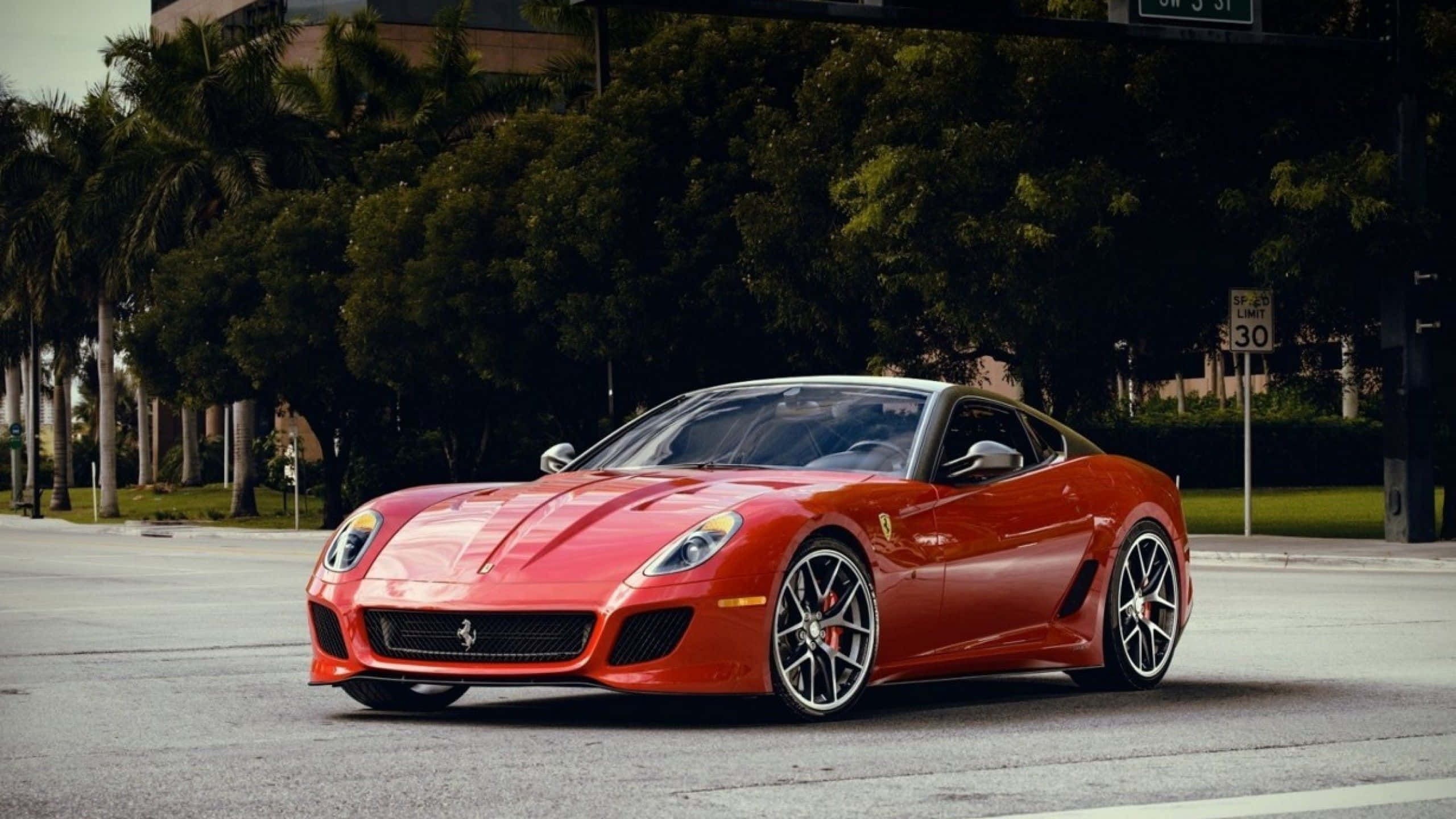 Ferrari 599 Gtb Fiorano 桌布 壁紙 — 一輛鮮紅色的法拉利跑車停泊在樹木成蔭的城市街道上，柔和日光下。