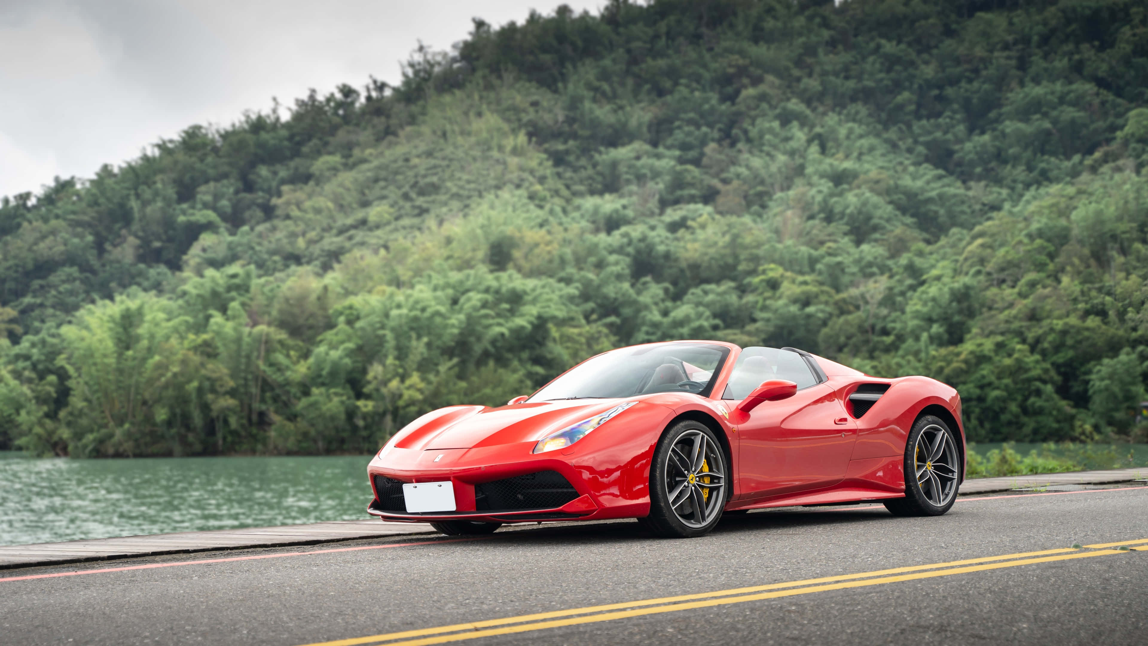 Ferrari 488 Spider 桌布 壁紙 — 一輛鮮紅色的法拉利跑車停泊在路邊，旁邊是一個平靜的湖泊，背景是鬱鬱蔥蔥的綠色山丘。