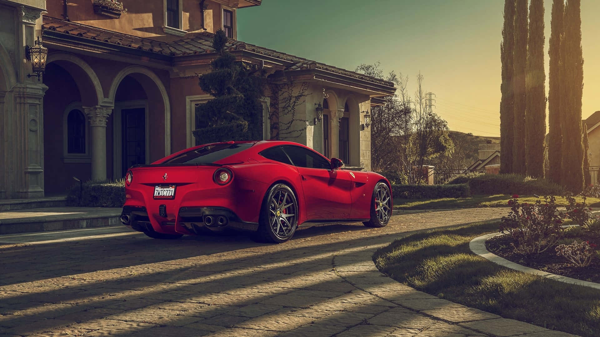 Ferrari F12 Berlinetta 桌布 壁紙 — 一輛鮮紅色的法拉利跑車停泊在陽光明媚的鵝卵石車道上，前面是一座豪華的地中海風格別墅。