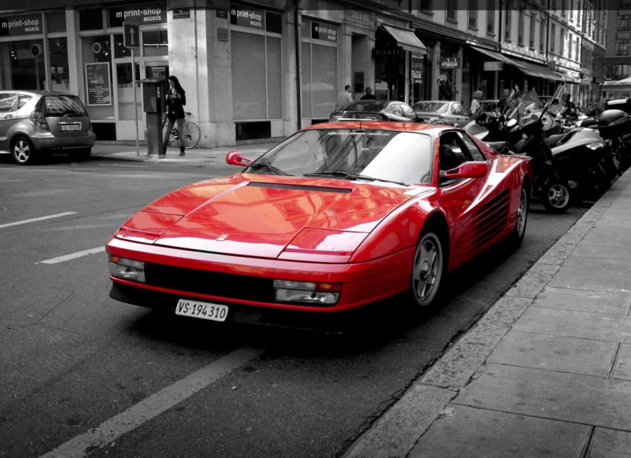 Ferrari Testarossa 桌布 壁紙 — 一輛鮮紅色的法拉利跑車停泊在黑白環境的城市街道上。