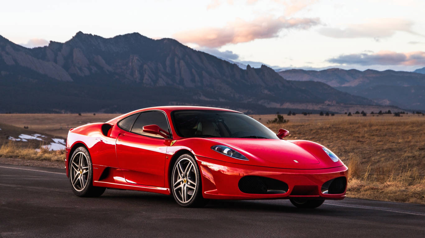 Sports Car 桌布 壁紙 — 一輛鮮紅色的法拉利跑車在日落時分沿著山路行駛，背景是崎嶇的山峰。