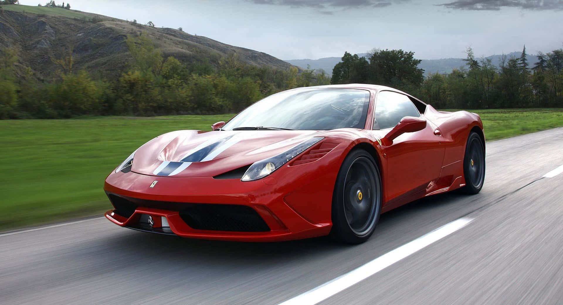 Ferrari 458 Speciale 桌布 壁紙 — 一輛鮮紅色的法拉利跑車在陰天之下，沿著蜿蜒的道路穿過鬱鬱蔥蔥的綠色山丘飛馳。