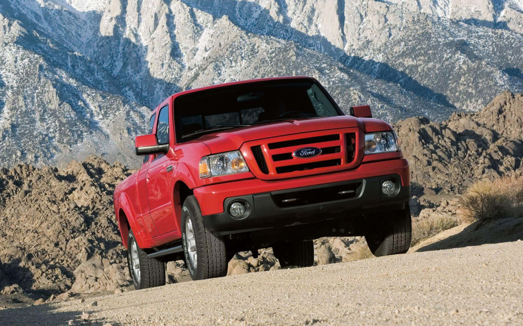 Ford Ranger 桌布 壁紙 — 一輛鮮紅色的福特皮卡車自信地行駛在岩石地形上，背後是白雪覆蓋的山脈。