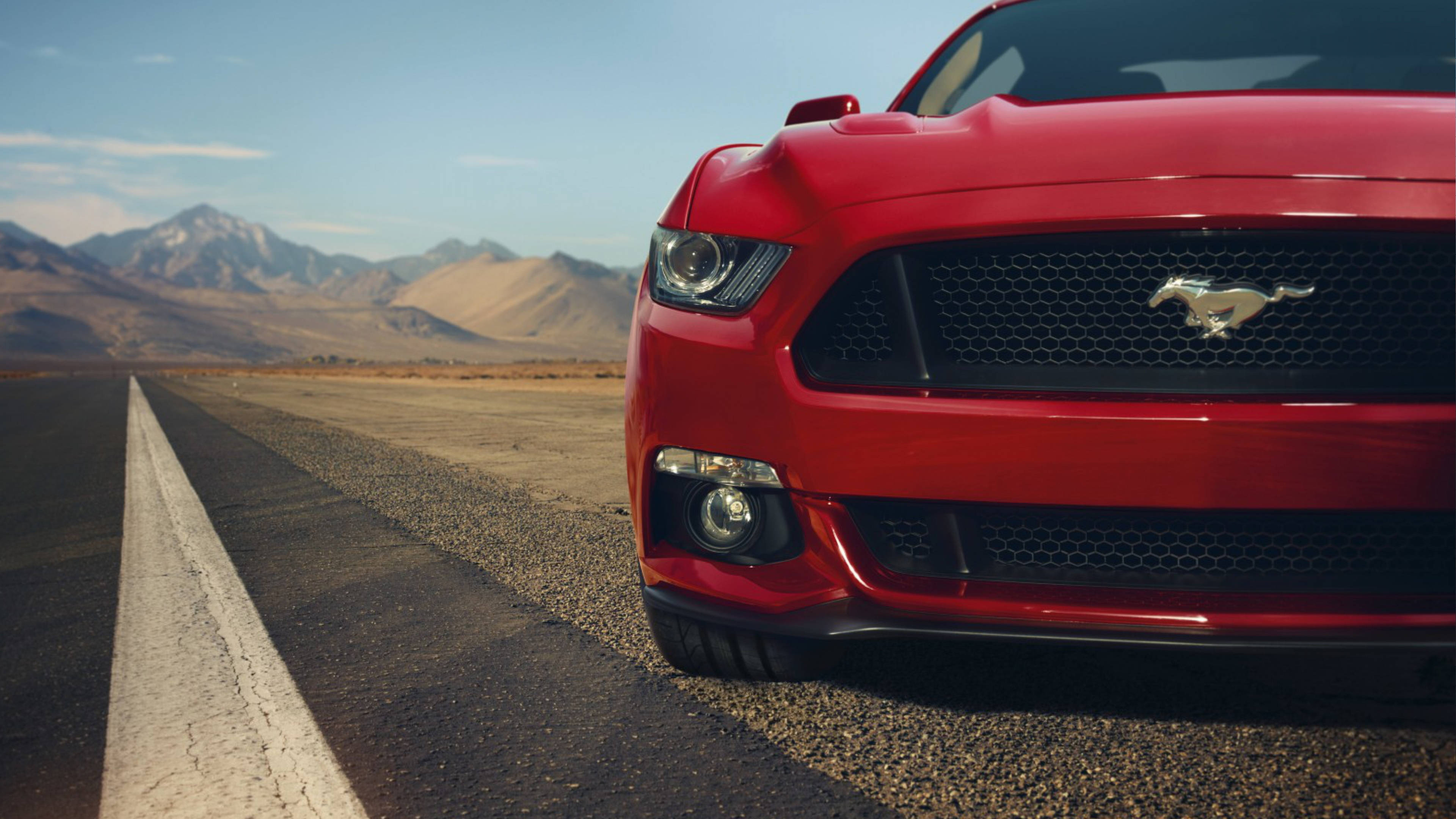 mustang HD 桌布 壁紙 — 一輛鮮紅色的福特野馬停泊在沙漠公路上，遠山在清澈的藍天下。