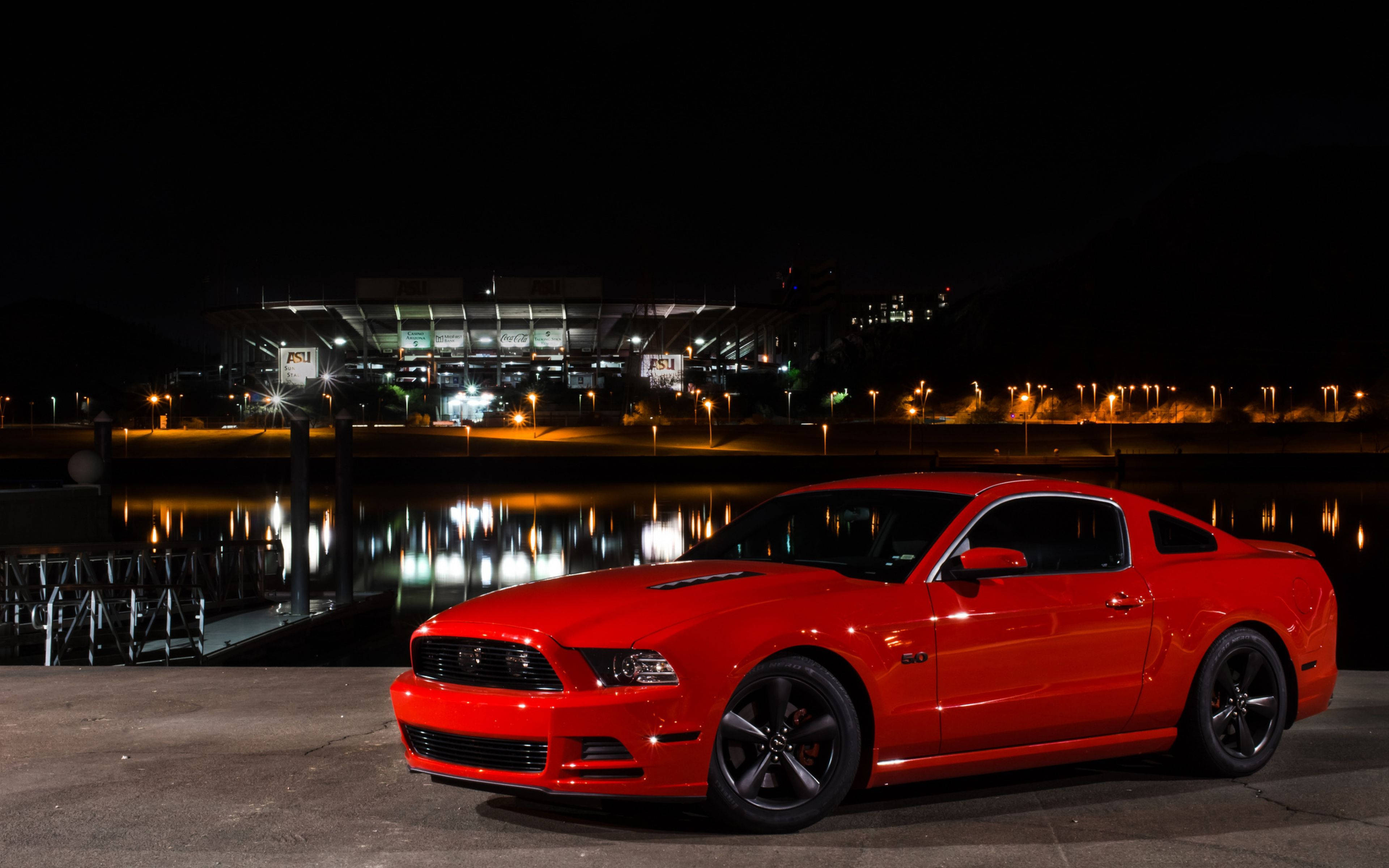 mustang HD 桌布 壁紙 — 一輛鮮紅色的福特野馬在夜燈下閃閃發光，旁邊平靜的水道倒映著遠處的體育場燈光。