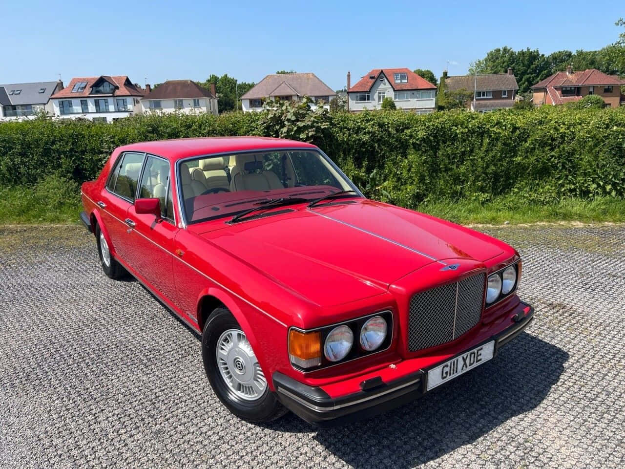 Bentley Eight 桌布 壁紙 — 一輛鮮紅色的經典 Bentley 房車在明亮的陽光下閃閃發光，停泊在碎石車道上，背景是郊區房屋和綠色籬笆。