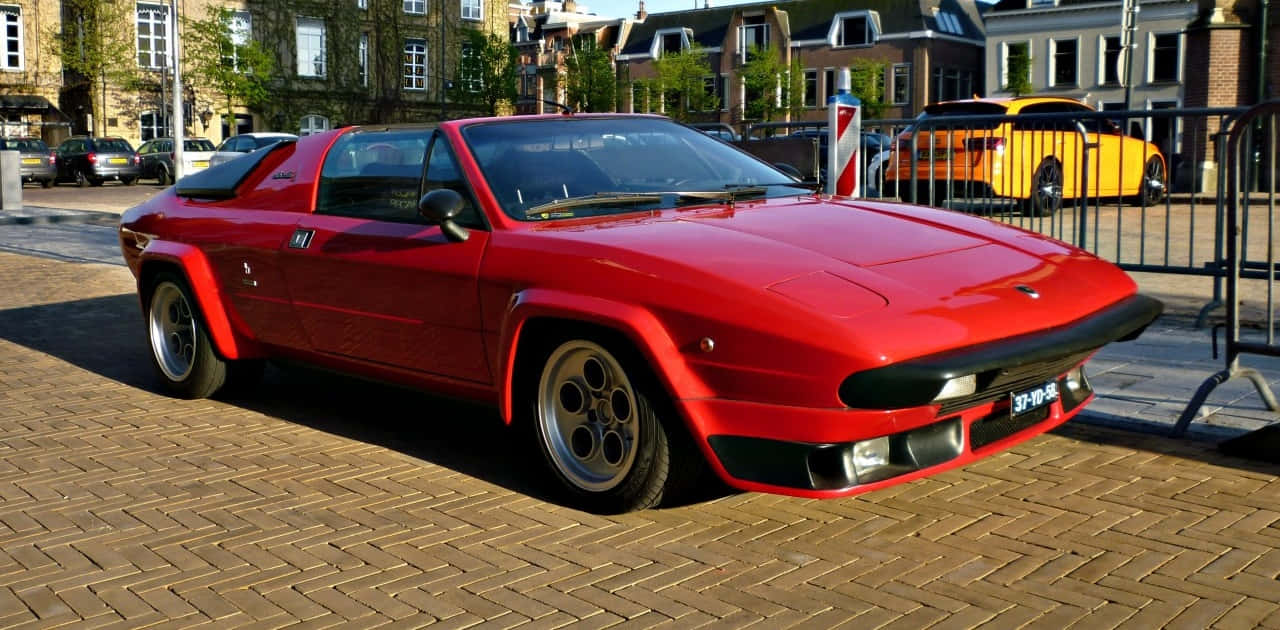 Lamborghini Silhouette 桌布 壁紙 — 一輛鮮紅色的經典跑車停泊在陽光普照的磚砌街道上，背景是歷史建築。