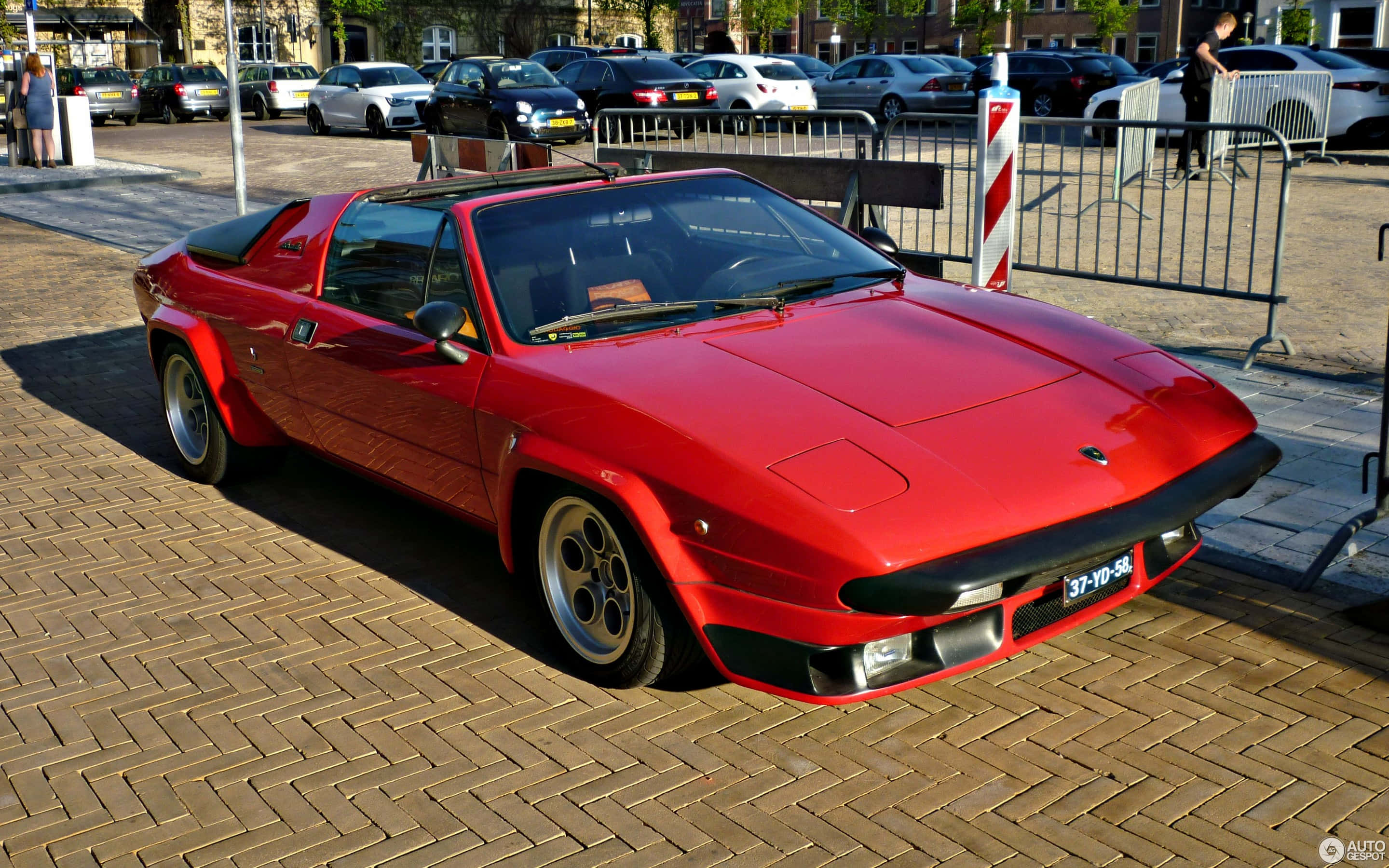 Lamborghini Silhouette 桌布 壁紙 — 一輛鮮紅色的經典跑車在明亮的陽光下閃閃發光，停放在磚砌的都市廣場上。