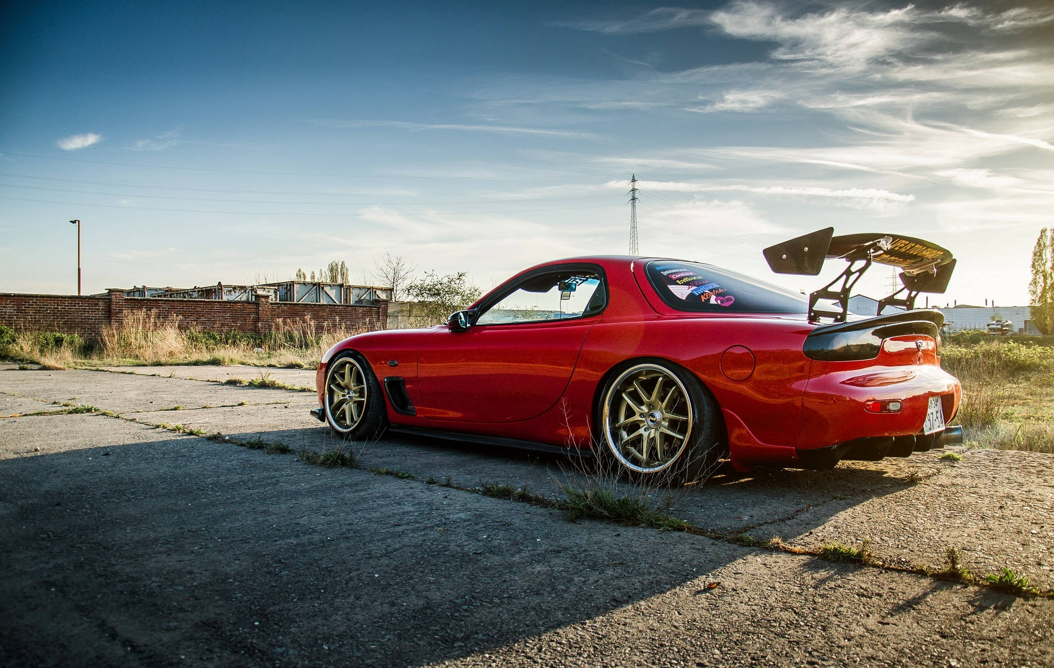 Mazda 桌布 壁紙 — 一輛鮮紅色的萬事得RX-7，帶有大型後擾流板，停在裂開的瀝青路面上，天空湛藍，薄雲飄逸。