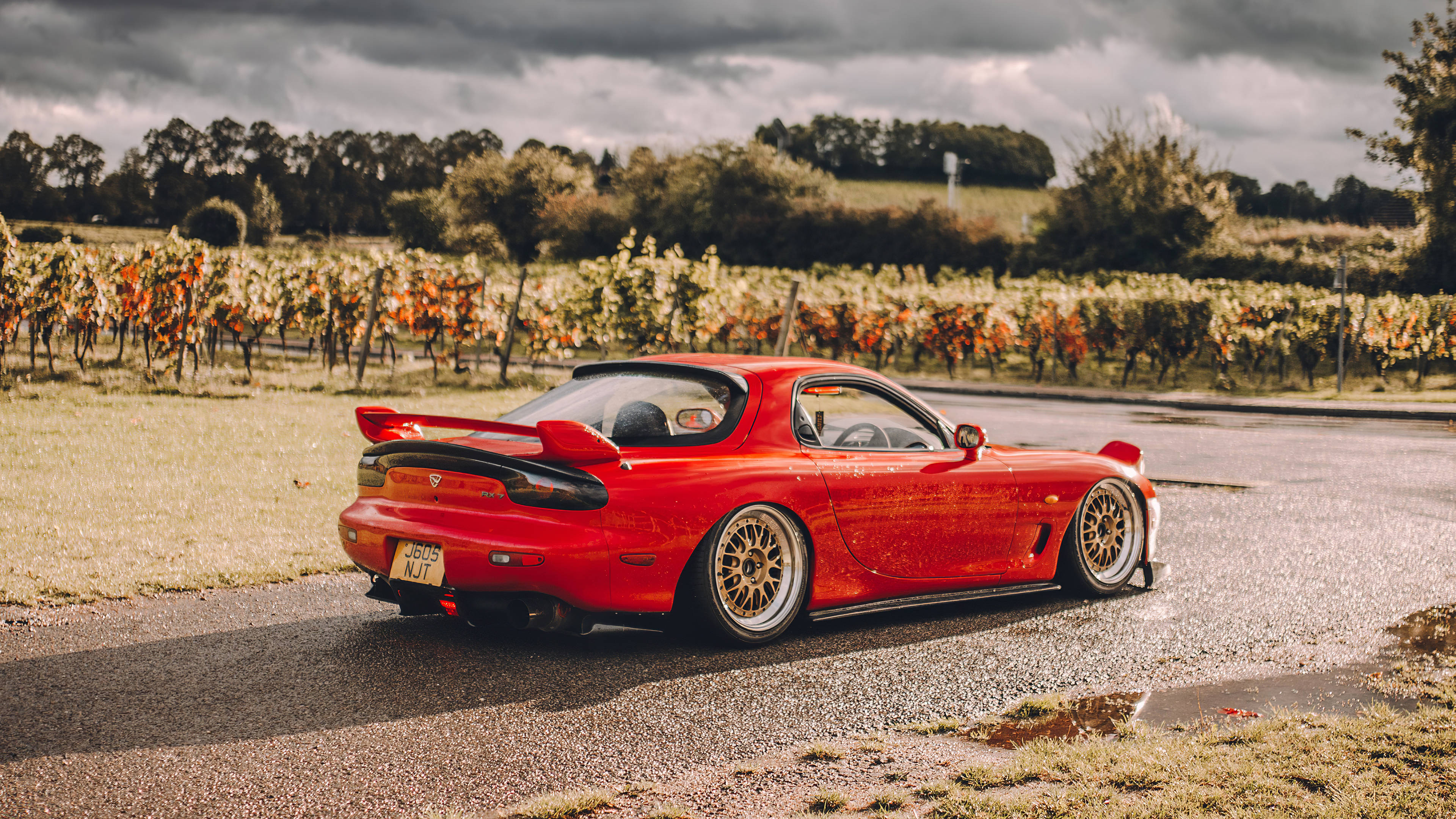 Mazda 桌布 壁紙 — 一輛鮮紅色的萬事得RX-7跑車停在潮濕的道路上，旁邊是秋天的葡萄園，天空多雲。