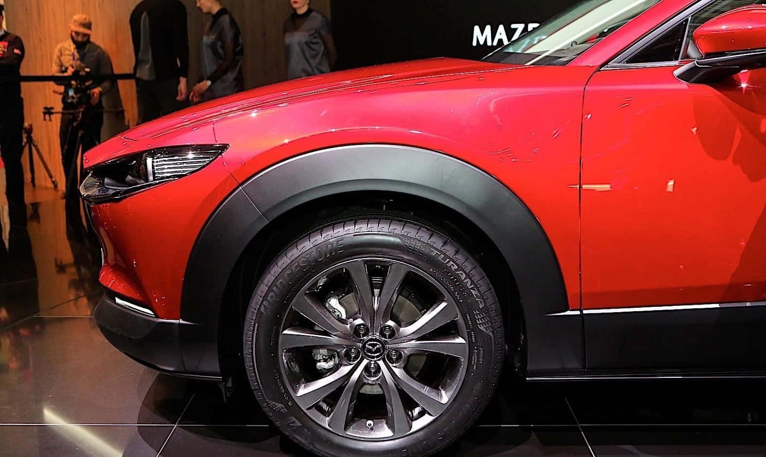 Mazda Cx-30 桌布 壁紙 — 一輛鮮紅色的萬事得SUV在車展的明亮燈光下閃閃發光，攝影師們捕捉其時尚設計。