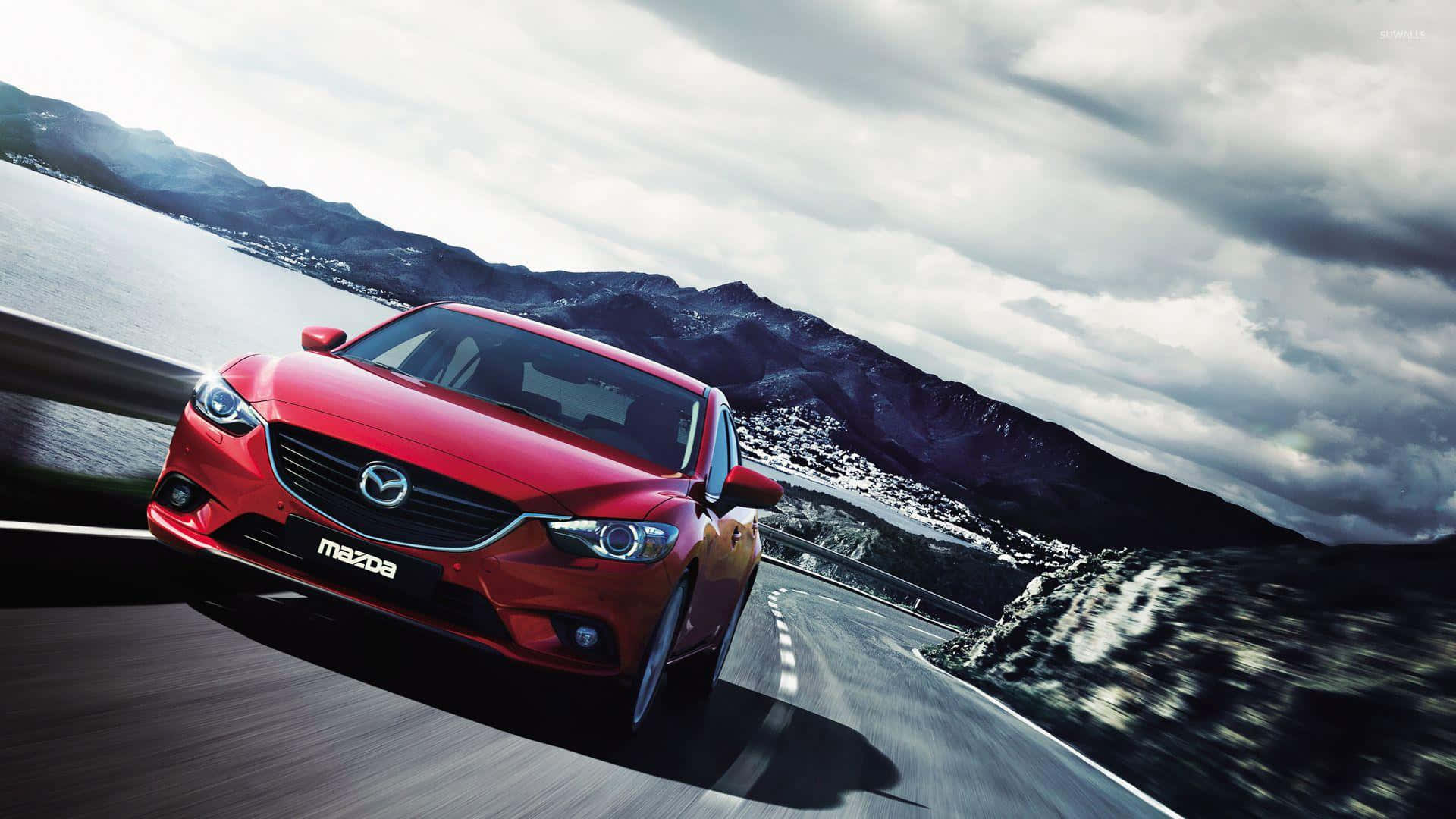 Mazda 6 桌布 壁紙 — 一輛鮮紅色的萬事得沿著蜿蜒的海岸道路疾馳，背景是山脈和多雲的天空。