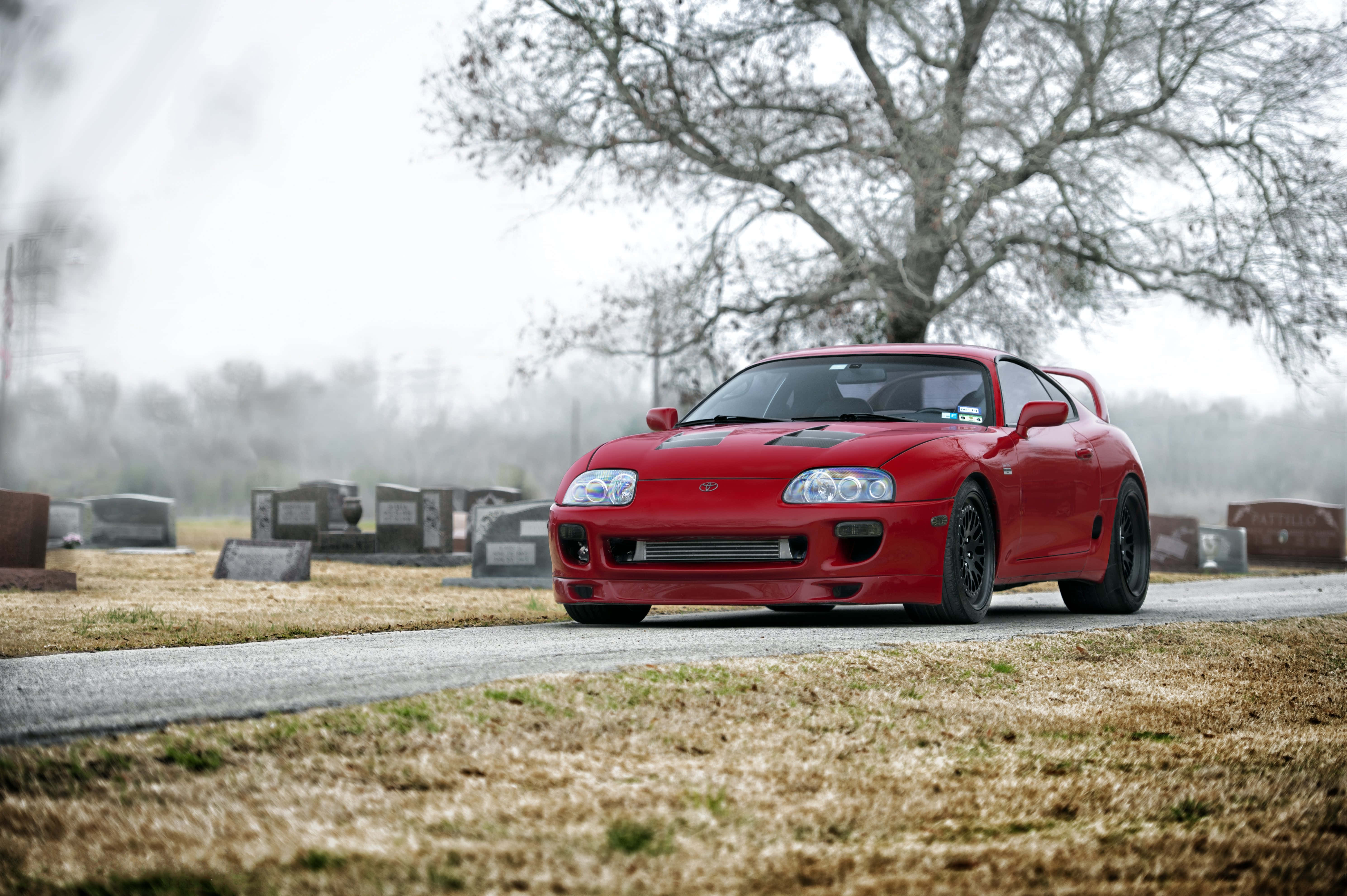 Supra 桌布 壁紙 — 一輛鮮紅色的豐田Supra跑車停泊在霧氣瀰漫的墓地小徑上，背景有光禿禿的樹木和墓碑。