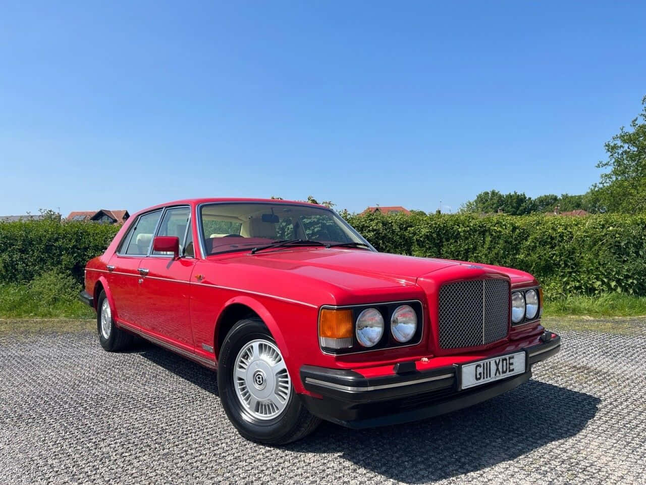 Bentley Eight 桌布 壁紙 — 一輛鮮紅色的賓利轎車在明亮的陽光下閃閃發光，停在碎石車道上，背景有綠色樹籬和藍天。