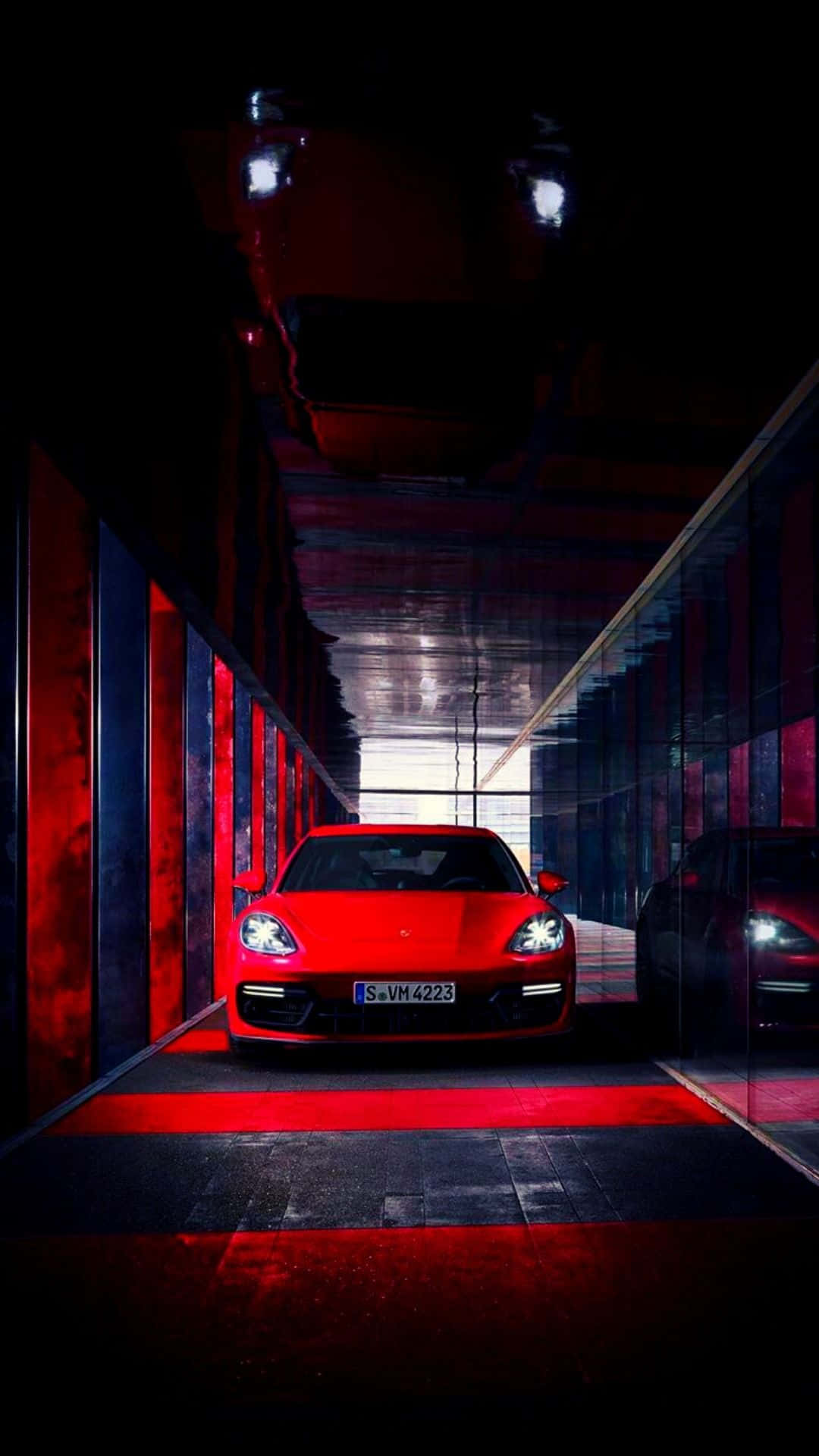 Porsche iPhone 桌布 壁紙 — 一輛鮮紅色的跑車在光滑現代、帶有反射表面的隧道中，於戲劇性的紅光照射下閃耀。