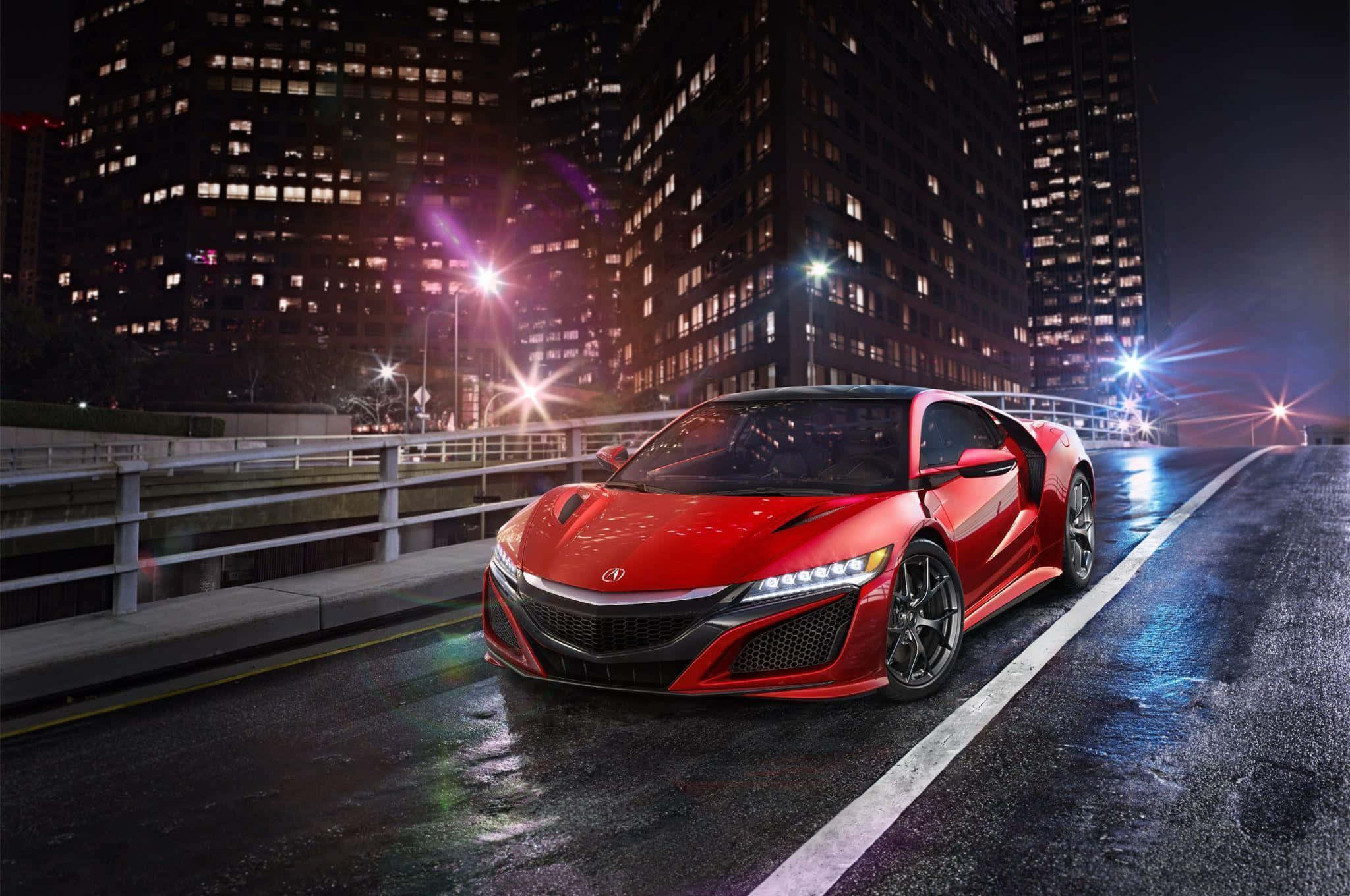 Acura Nsx 桌布 壁紙 — 一輛鮮紅色的跑車在夜間濕滑的城市街道上滑行，被耀眼的街燈和高聳的摩天大樓照亮。