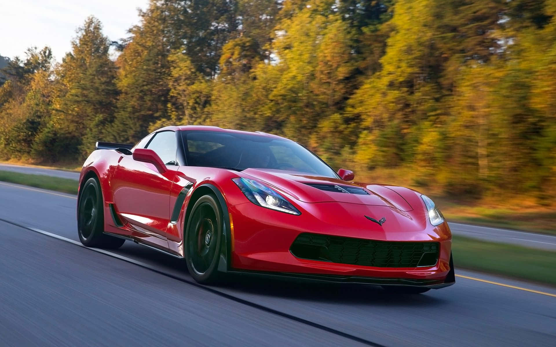Chevrolet Corvette Z06 桌布 壁紙 — 一輛鮮紅色的跑車在樹林環繞的道路上疾馳，動態模糊傳達出高速感。
