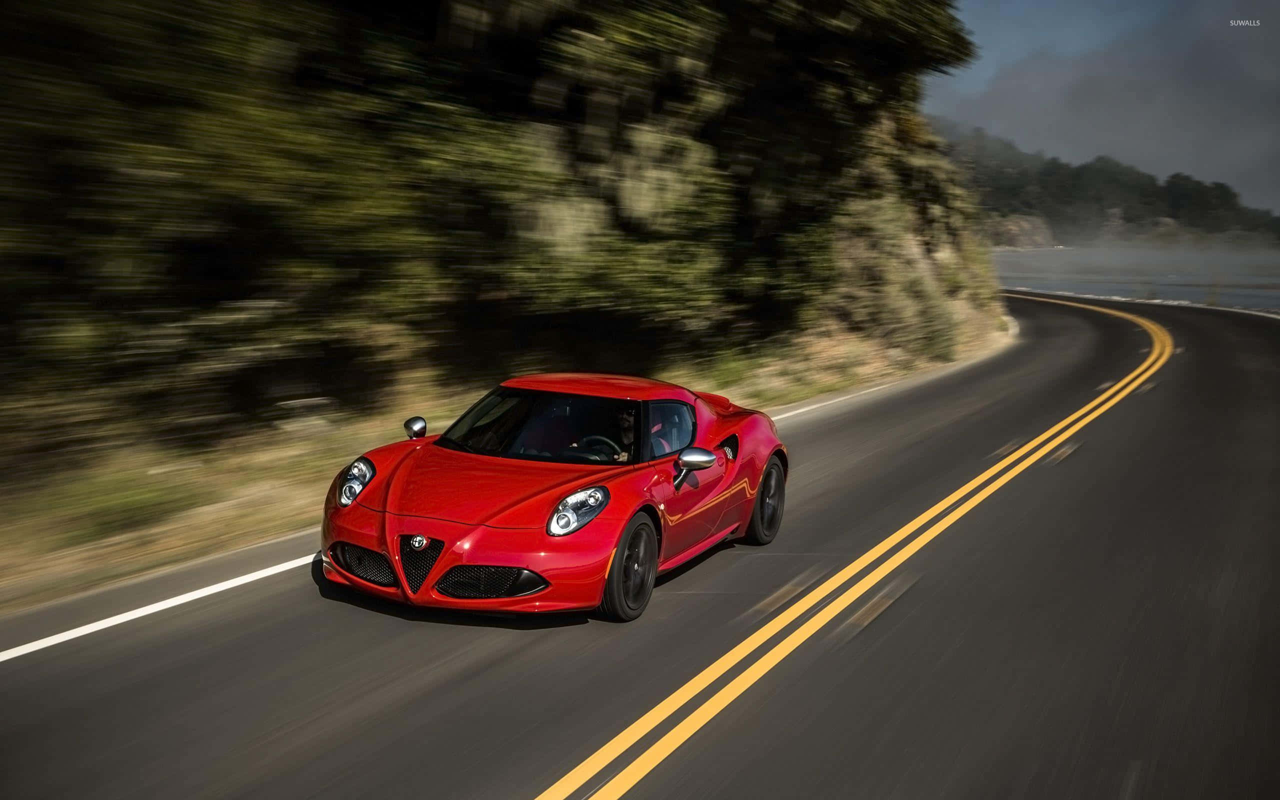 Alfa Romeo 4c 桌布 壁紙 — 一輛鮮紅色的跑車沿著蜿蜒的海岸道路飛馳，背景是模糊的綠樹和海洋。